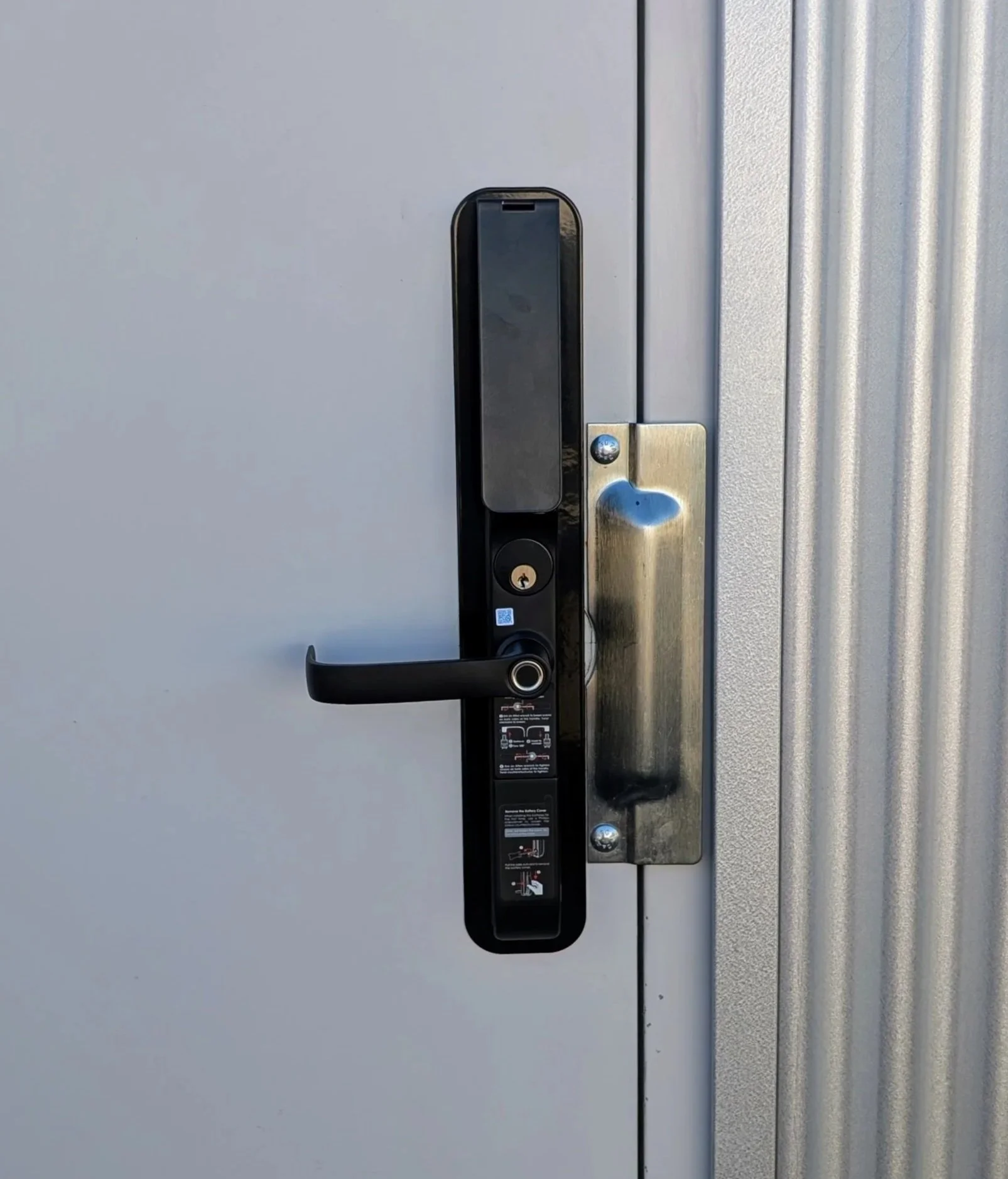 A close-up of a modern door handle and lock on a gray metal door.