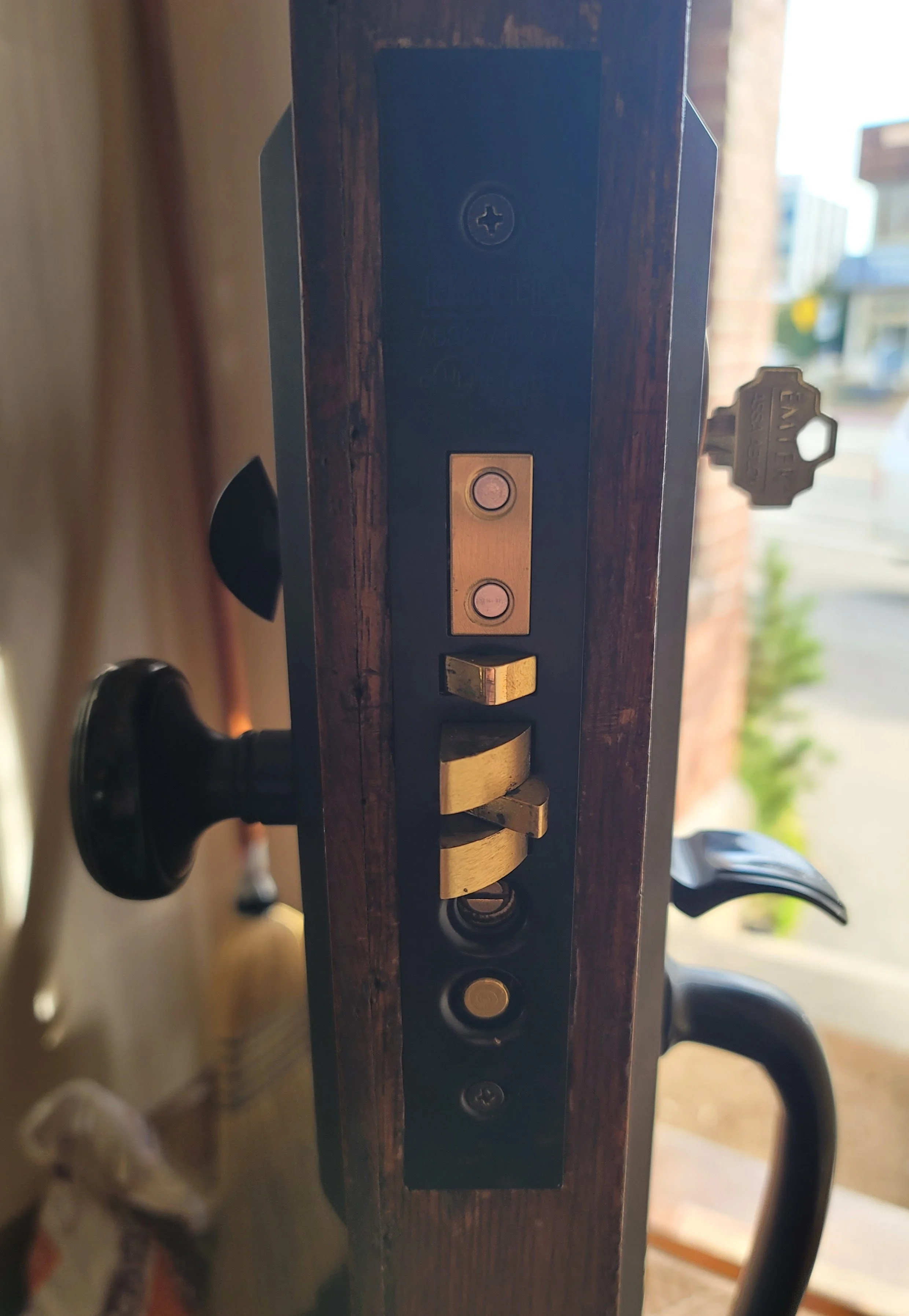 Close-up of a door lock with a handle and a key inserted into the lock mechanism. The lock appears old with visible mechanisms.
