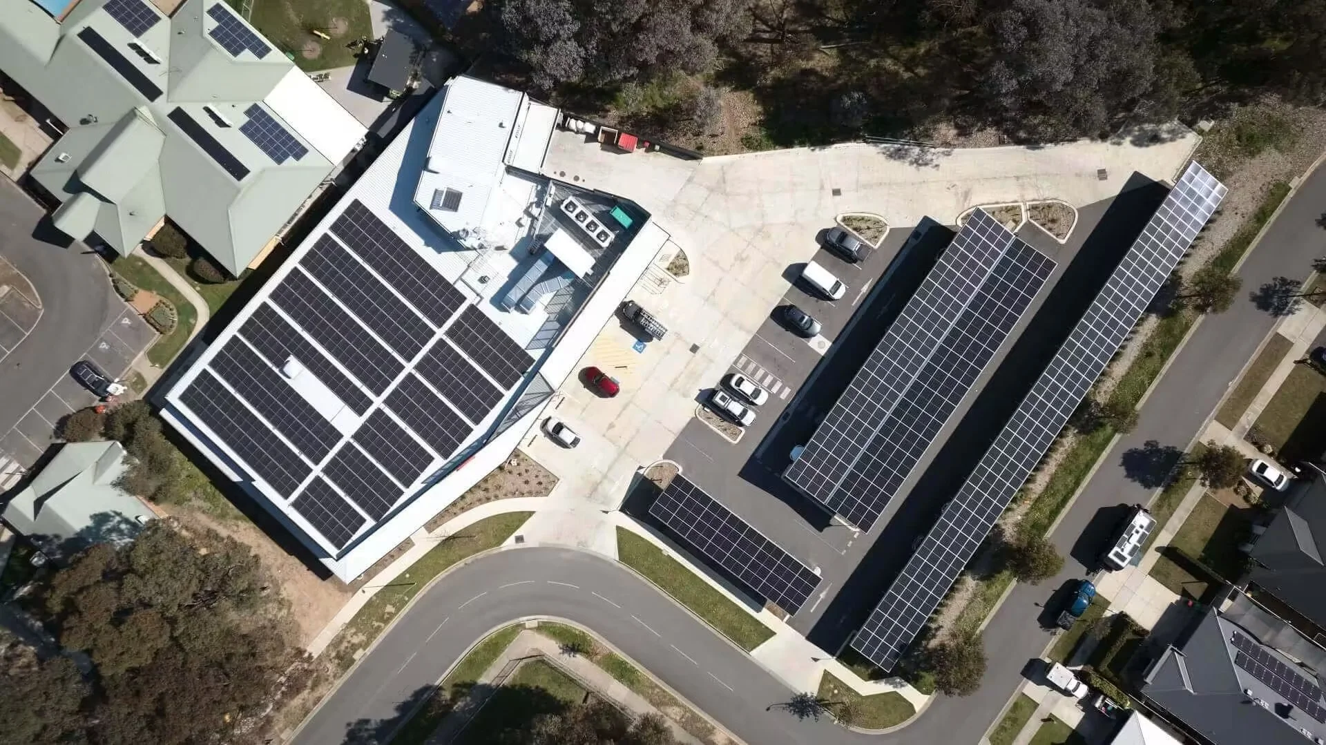 An aerial view of buildings with solar panels on the roofs, parking lots, and surrounding trees.