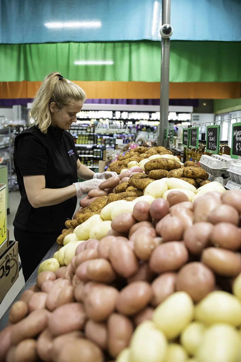 A woman shopping for potatoes in a grocery store produce aisle.