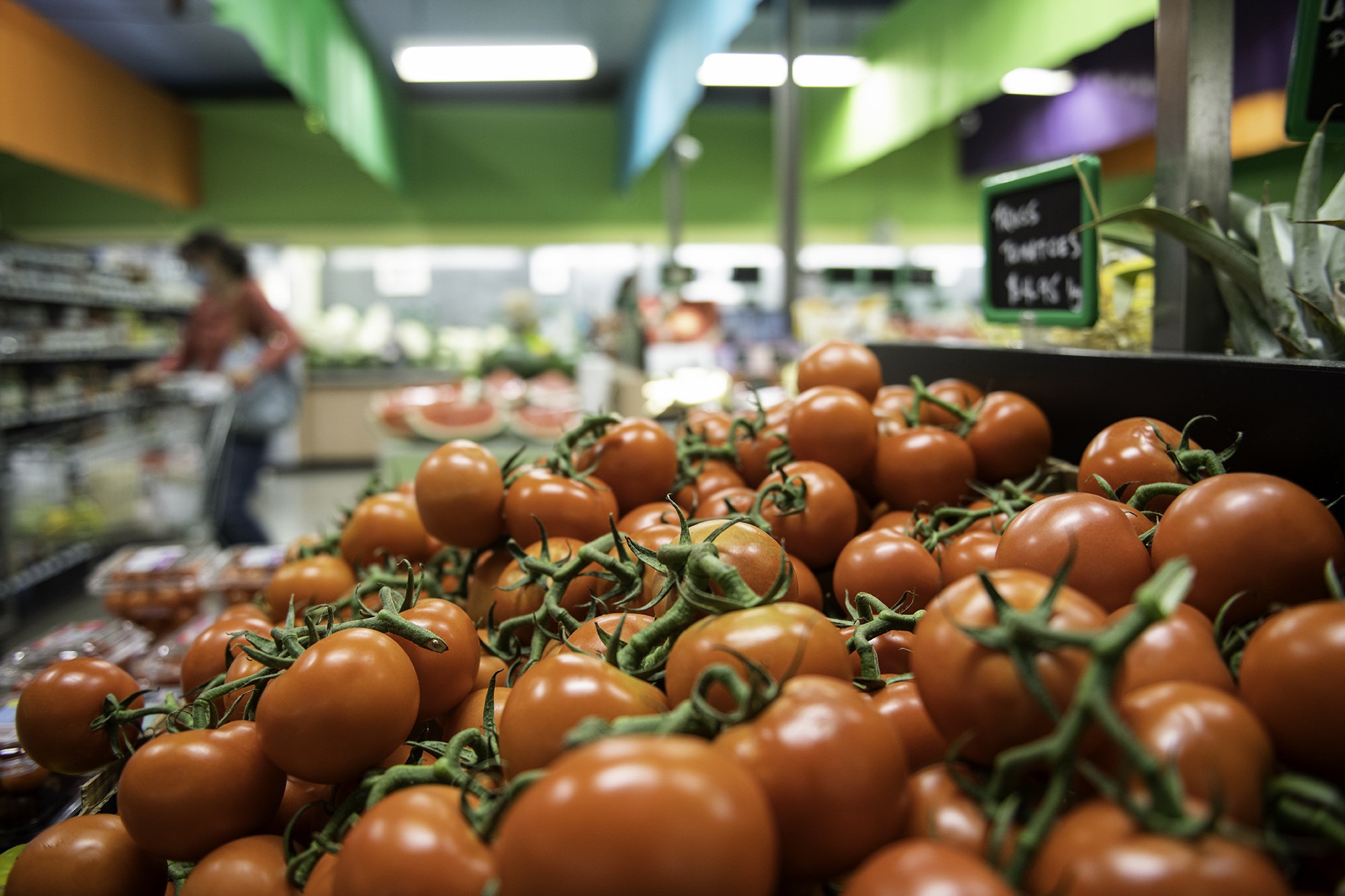 A display of fresh orange tomatoes at a grocery store produce section.