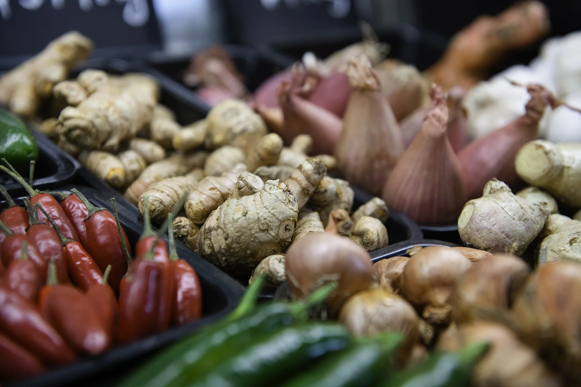 Fresh red chili peppers, ginger, sweet potatoes, onions, carrots, and white garlic on display at a grocery store.