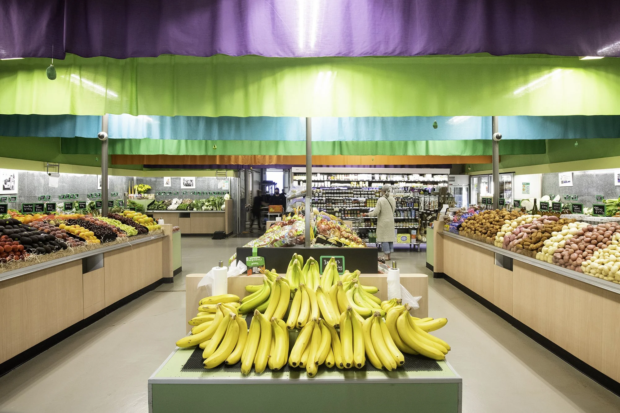 Display of fresh bananas in the produce section of a grocery store with colorful hanging fabric decor overhead.