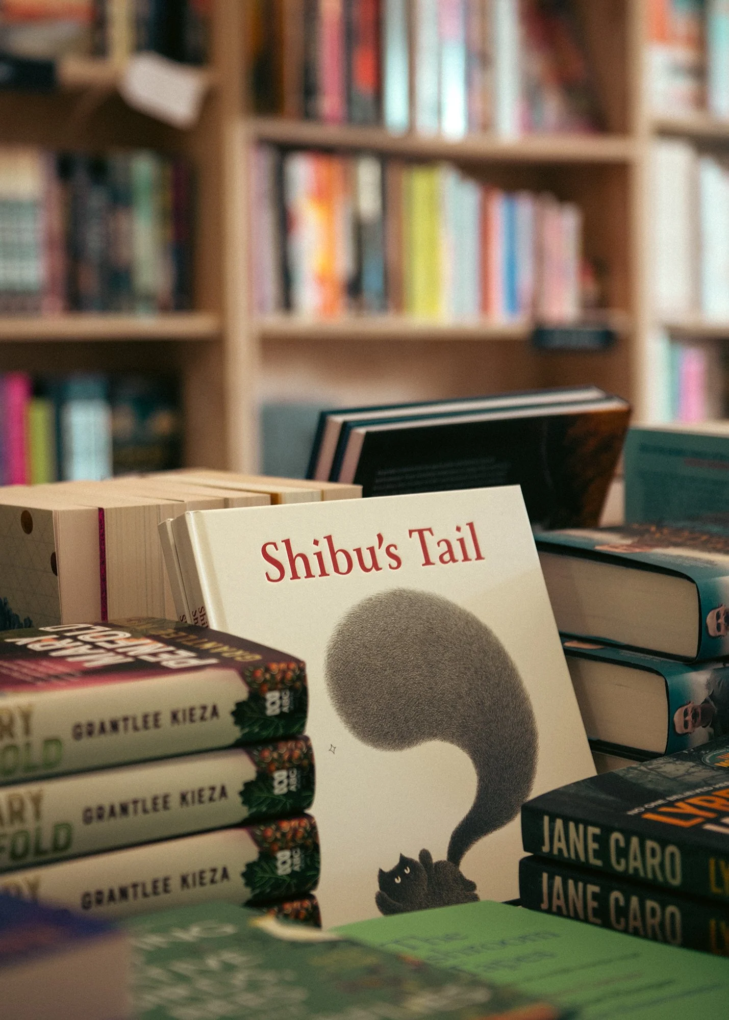 Close-up of a stack of books on a table in front of a bookshelf filled with various books.