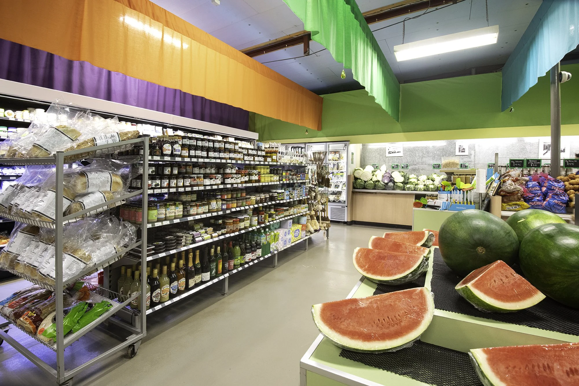 Display of sliced watermelons in a grocery store with other fruits and shelves of various food products in the background.