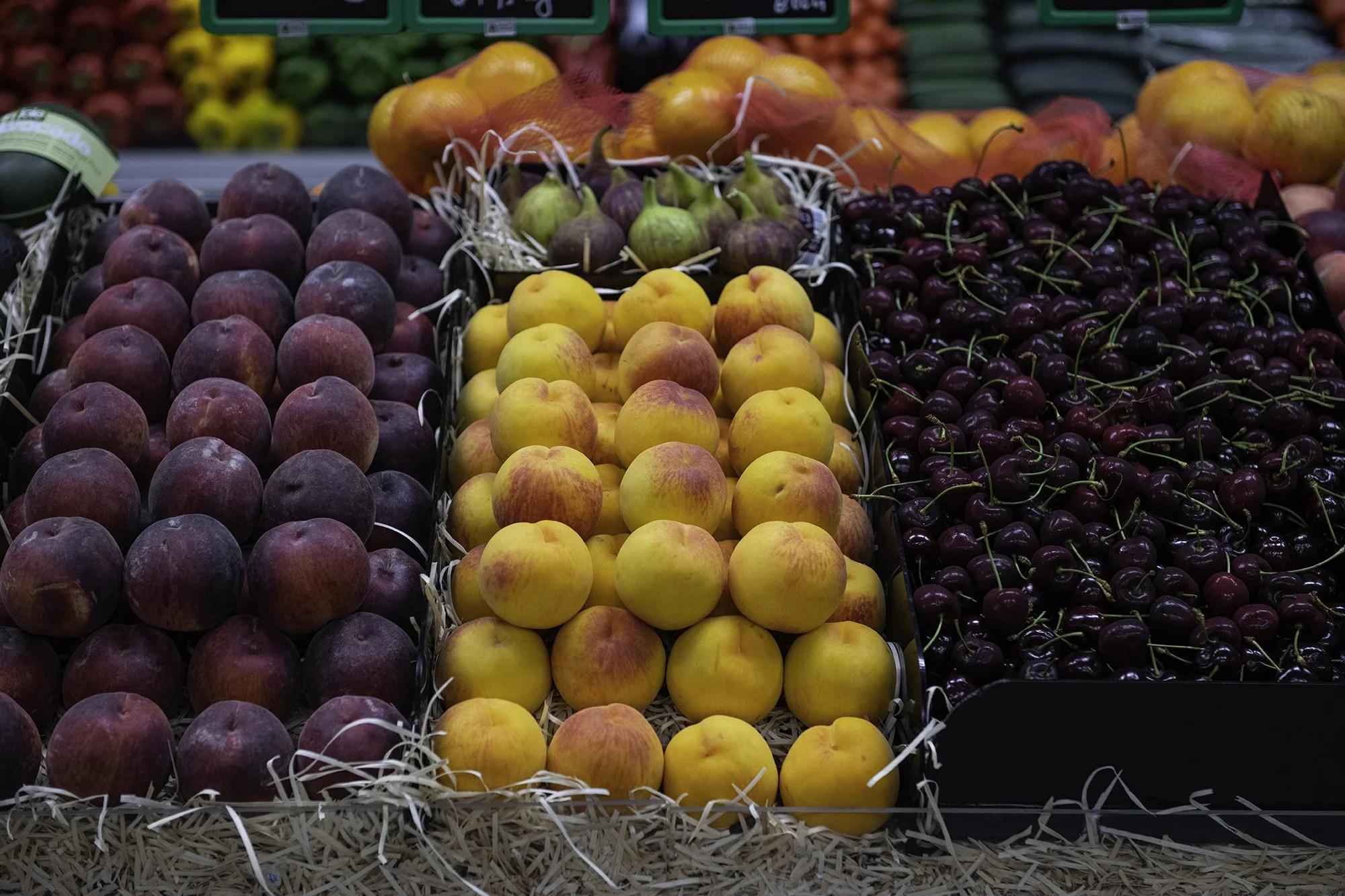 Display of fresh peaches, nectarines, and cherries in baskets at a grocery store produce section.