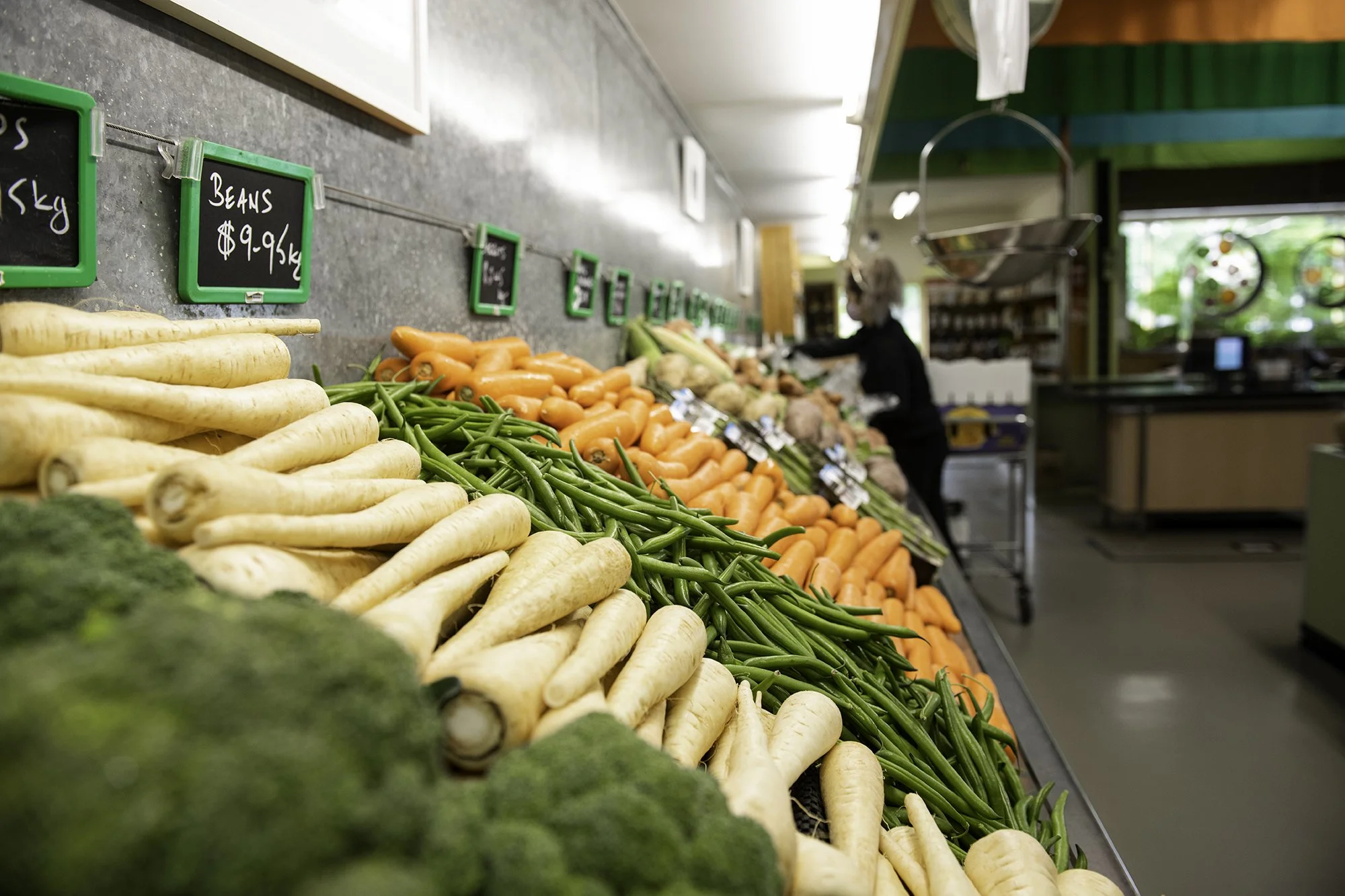 Display of fresh vegetables, including parsnips, green beans, carrots, and broccoli, arranged on a market stall with price tags.
