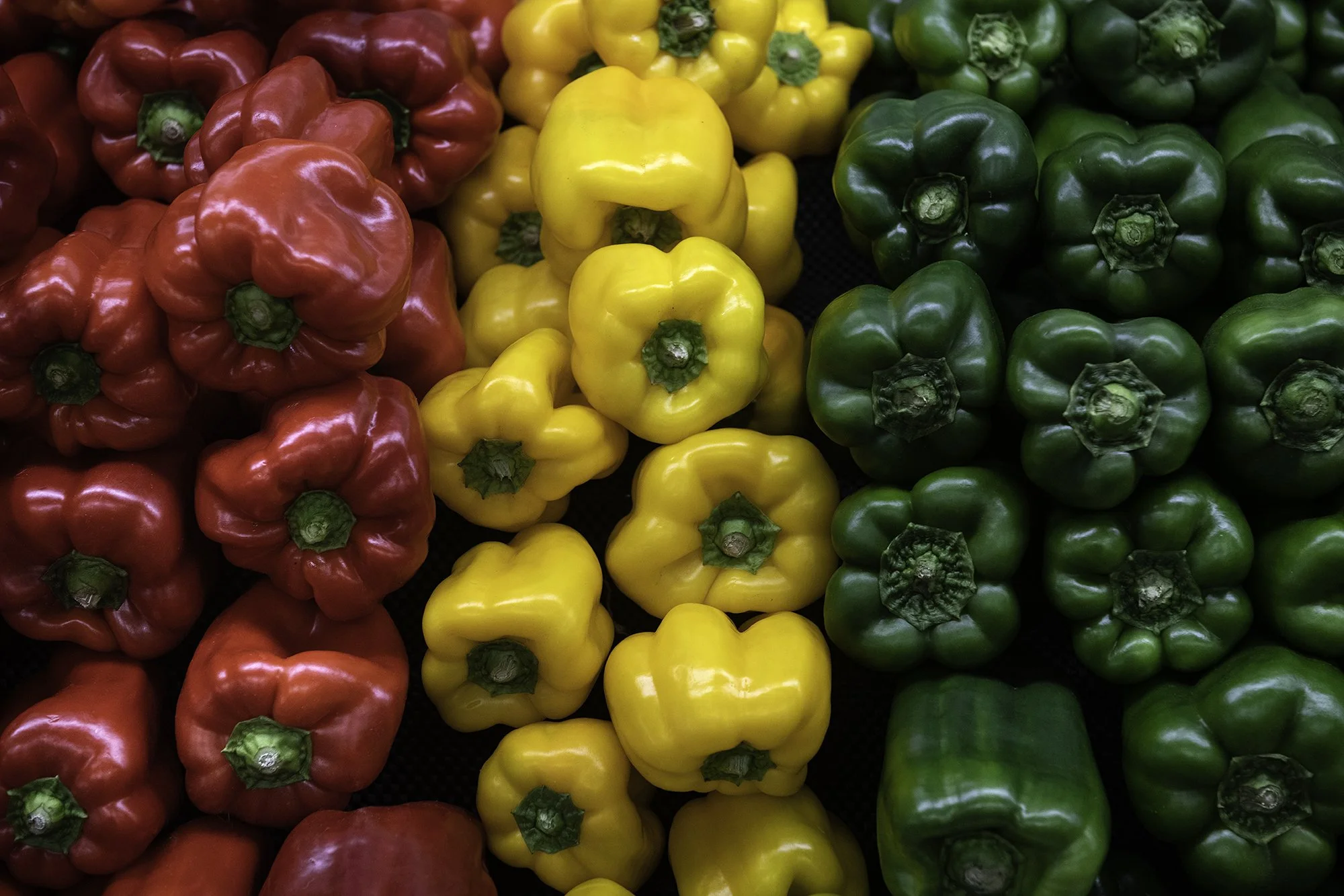 A display of red, yellow, and green bell peppers arranged in rows.