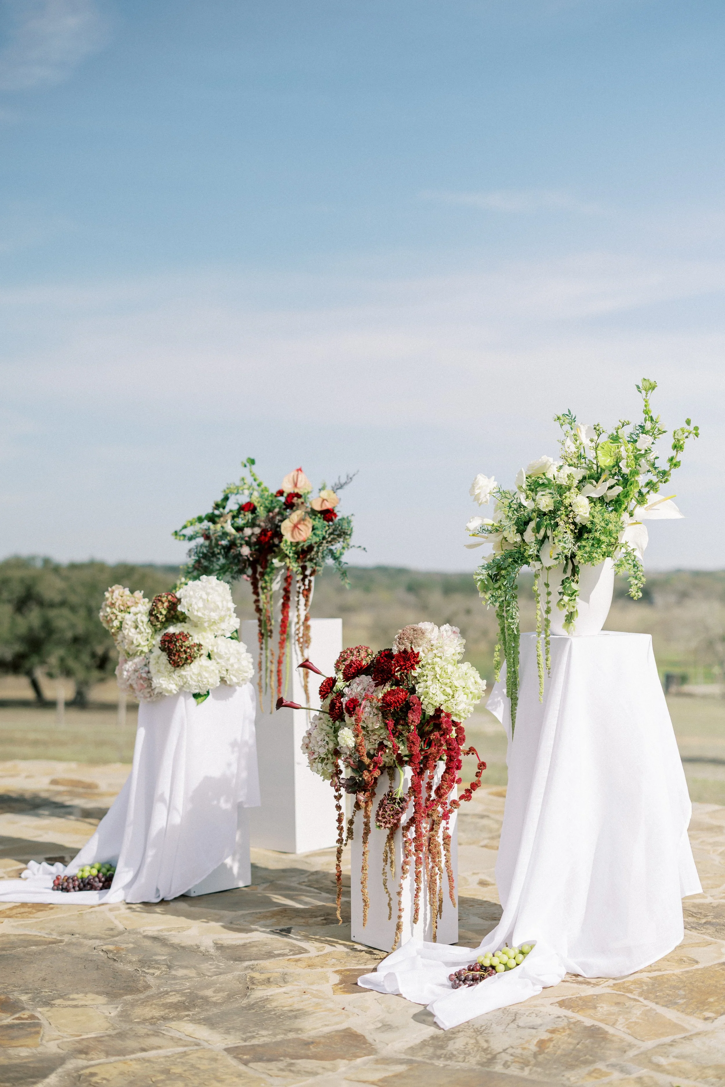 Arrangement of white and colorful flowers on white stands outdoors against a clear blue sky.