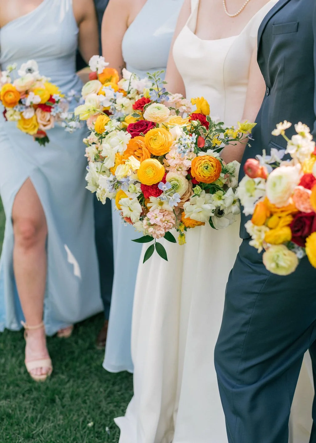 Bridgarly dressed wedding party holding colorful bouquets of flowers at an outdoor wedding.