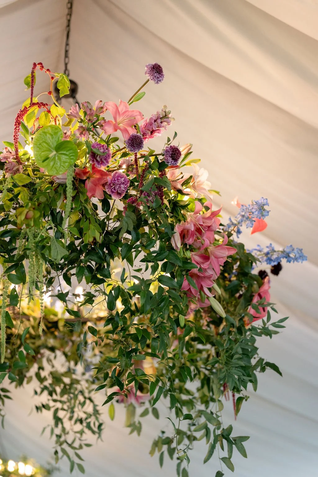 A colorful hanging floral arrangement with pink, purple, blue, and green flowers and foliage, hanging from a ceiling with a chain.