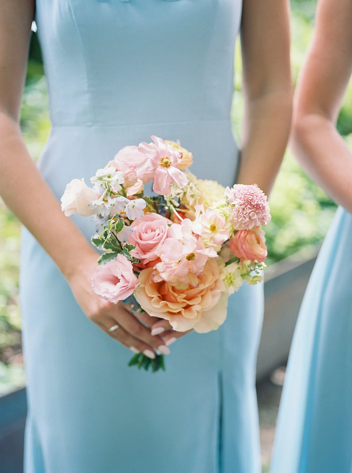 Person in a blue dress holding a bouquet of pink, white, and peach flowers outdoors.
