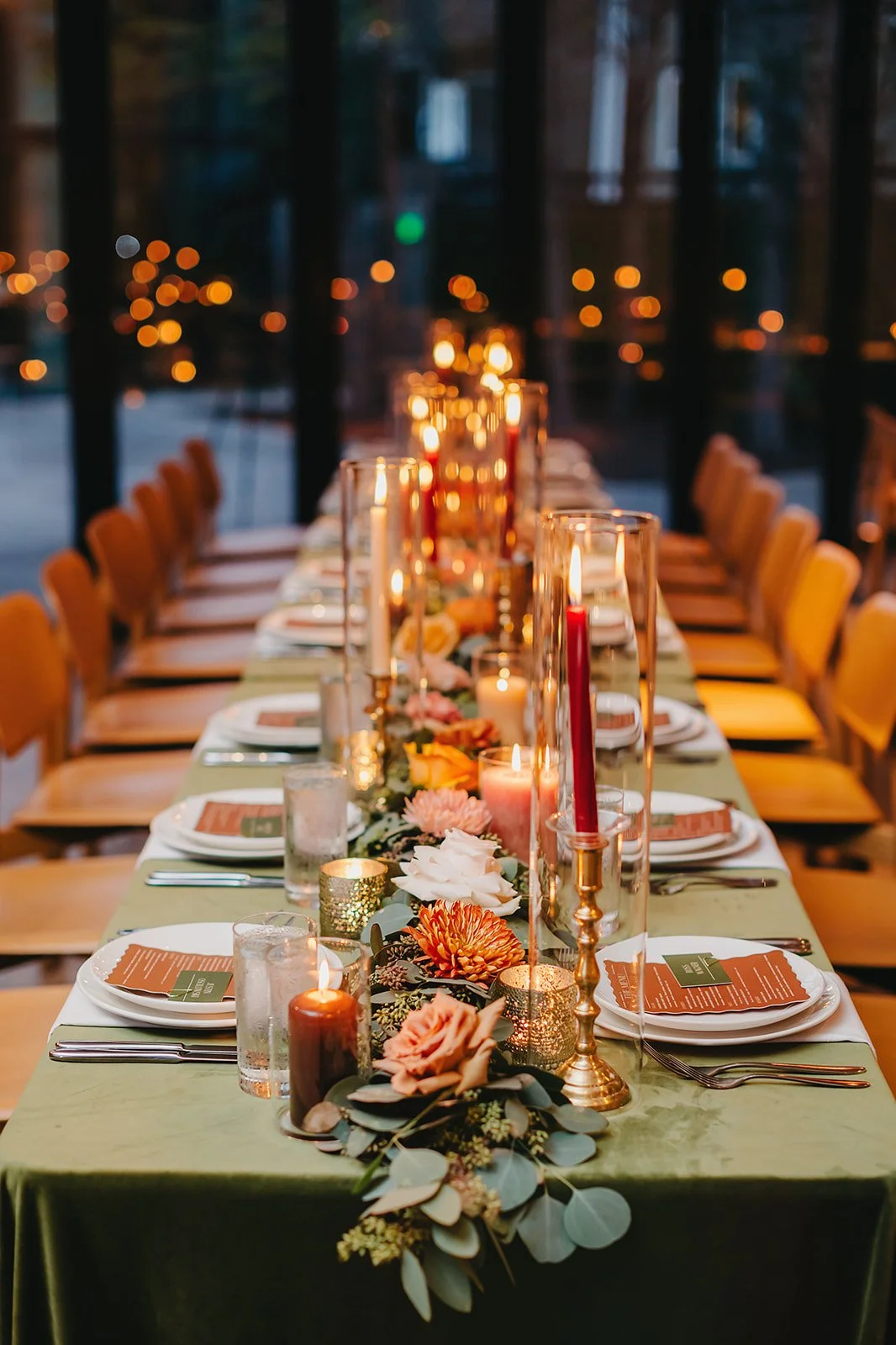 Elegant dining table set with candles, flowers, and glassware in a warmly lit restaurant