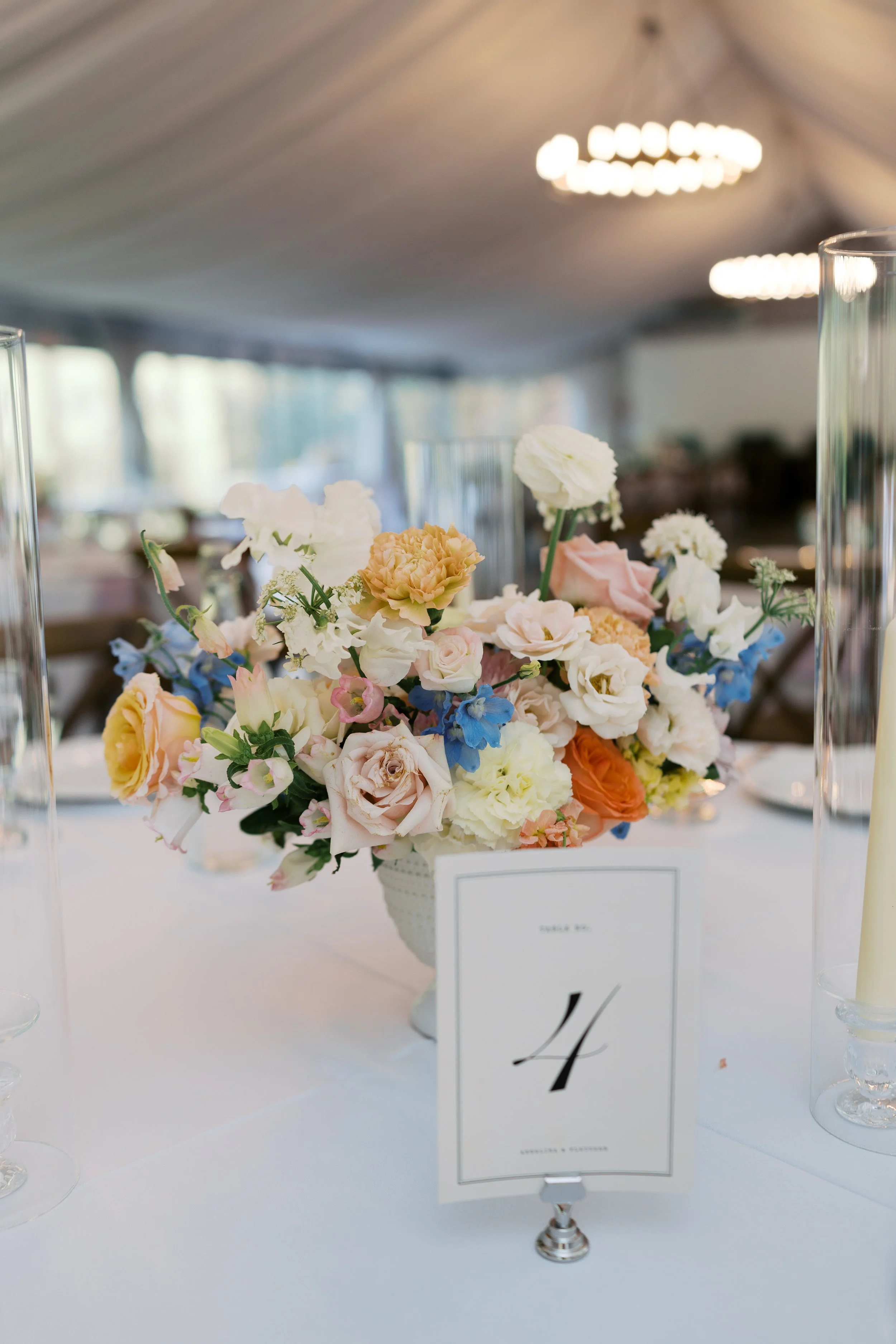 Close-up of a floral centerpiece with pastel-colored flowers on a white table at an event, with a table number card labeled '4' in front.