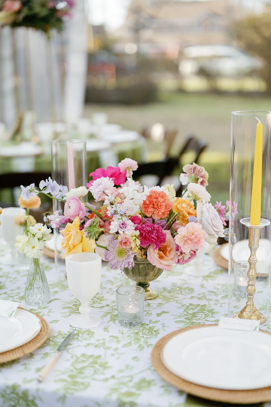 Elegant outdoor table setting with a floral centerpiece, candles, and dinnerware for a celebration or event.