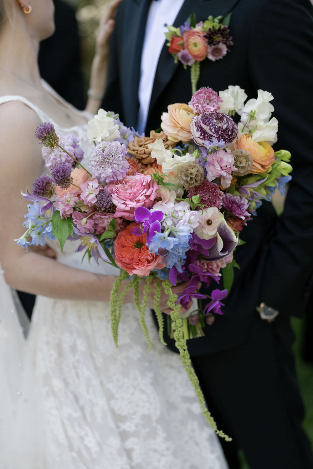 A bride and groom holding a large, colorful bouquet of various flowers at their wedding.