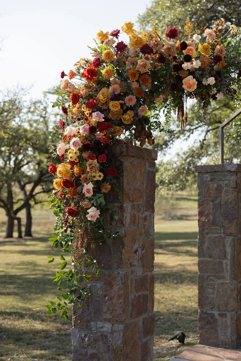 Colorful floral arrangement with roses, dahlias, and other flowers on top of stone pillars outdoors.