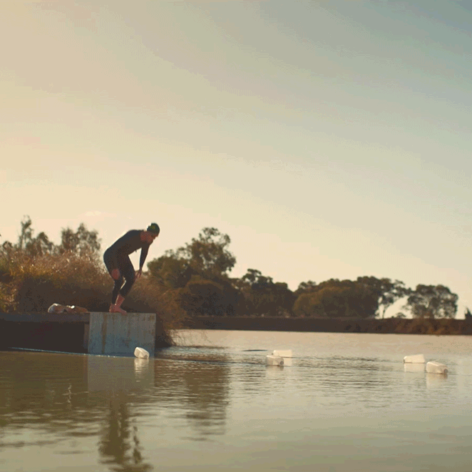 Person preparing to jump into a body of water from a concrete ledge during sunset