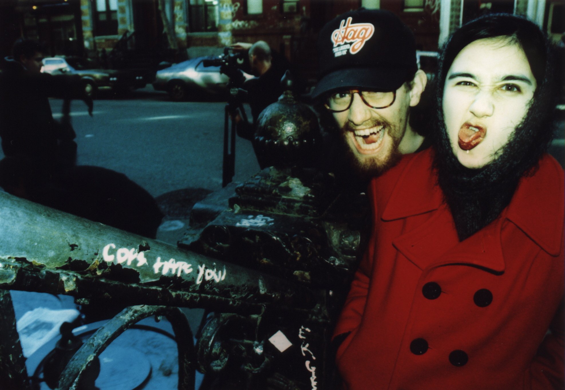 Candid shot of independent film actor and punk singer and actress on set of indie movie 'Threat' next to graffiti that reads 'Cops hate you' in 1990s New York City