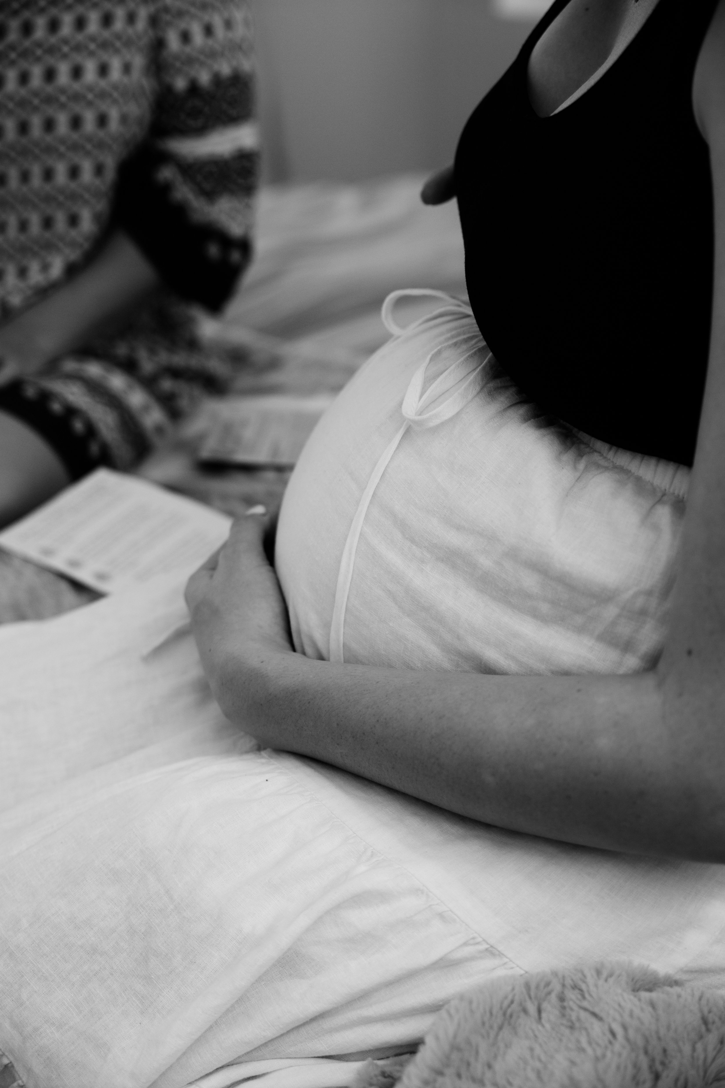 Black and white photo of a pregnant woman sitting on a bed.