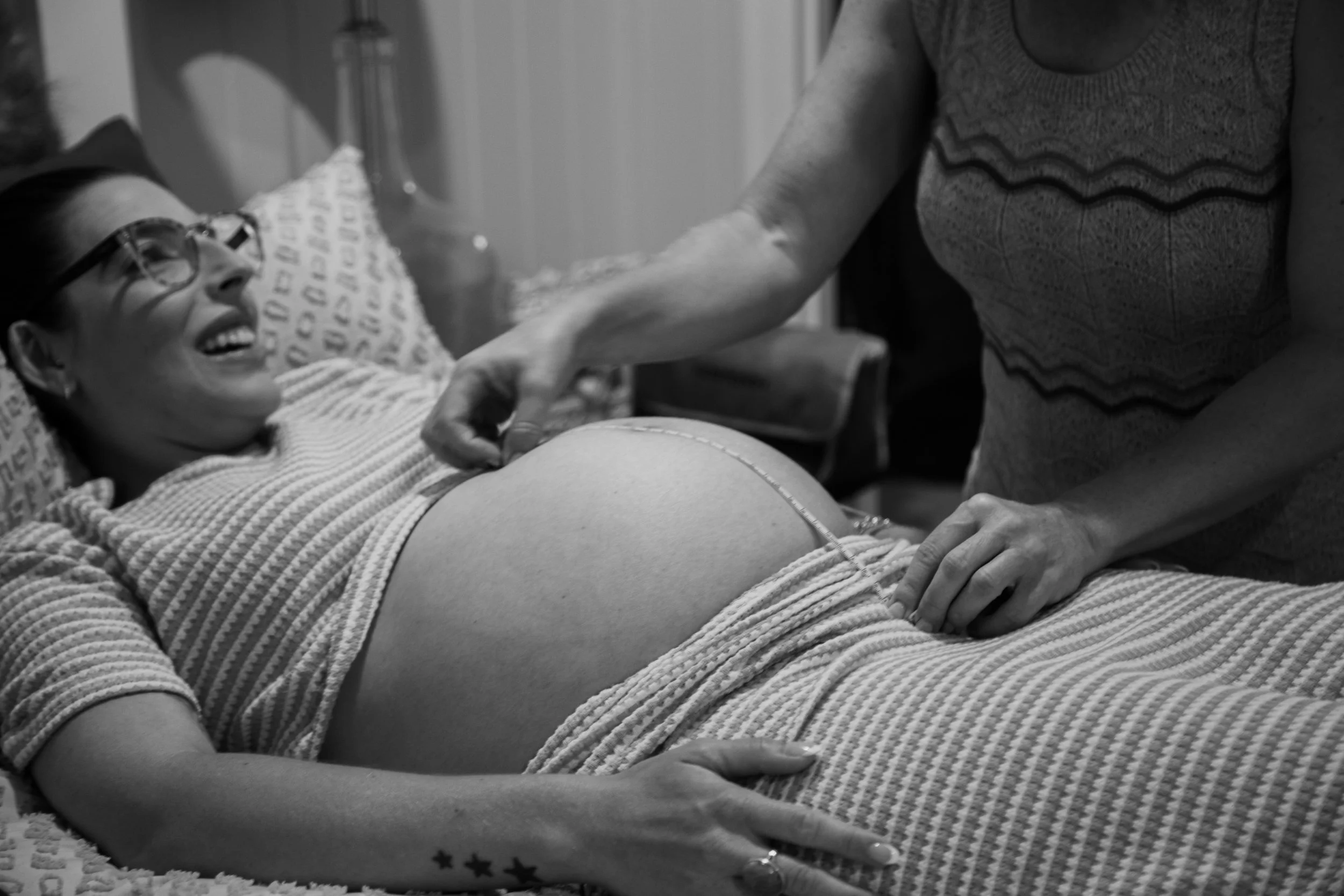 A woman lying in bed smiling, having her pregnant belly measured.