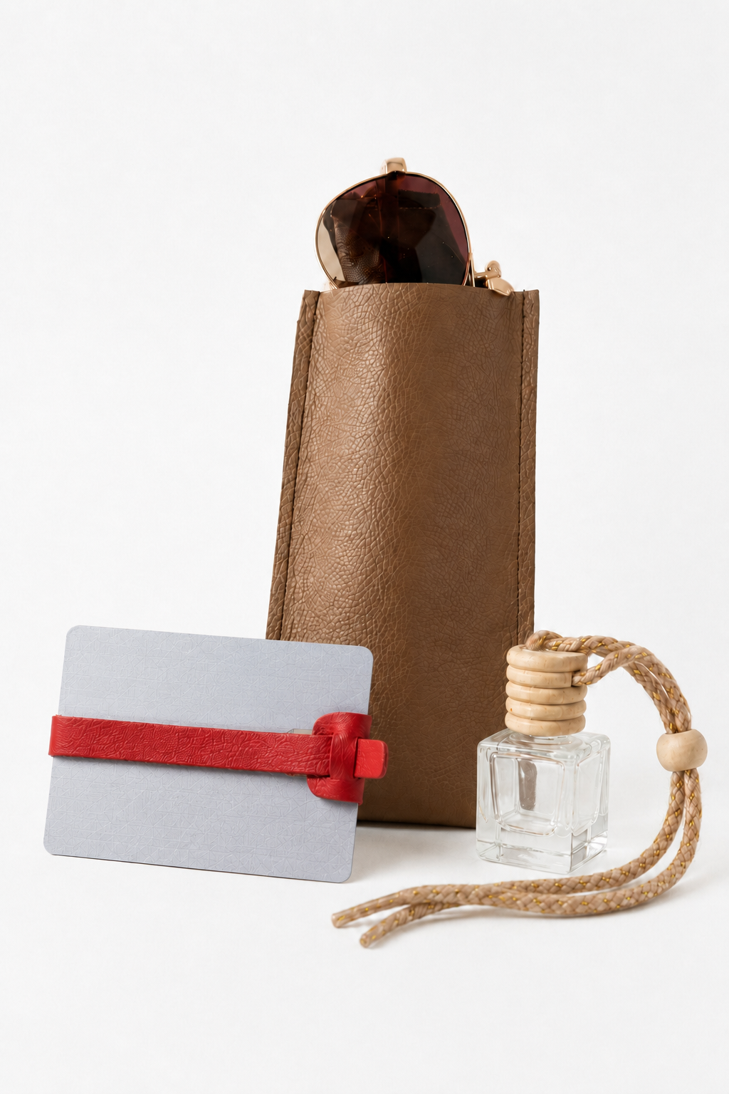A collection of accessories including a brown textured pouch with sunglasses inside, a white card with a red strap, and a clear glass perfume bottle with a beige cord and wooden bead.