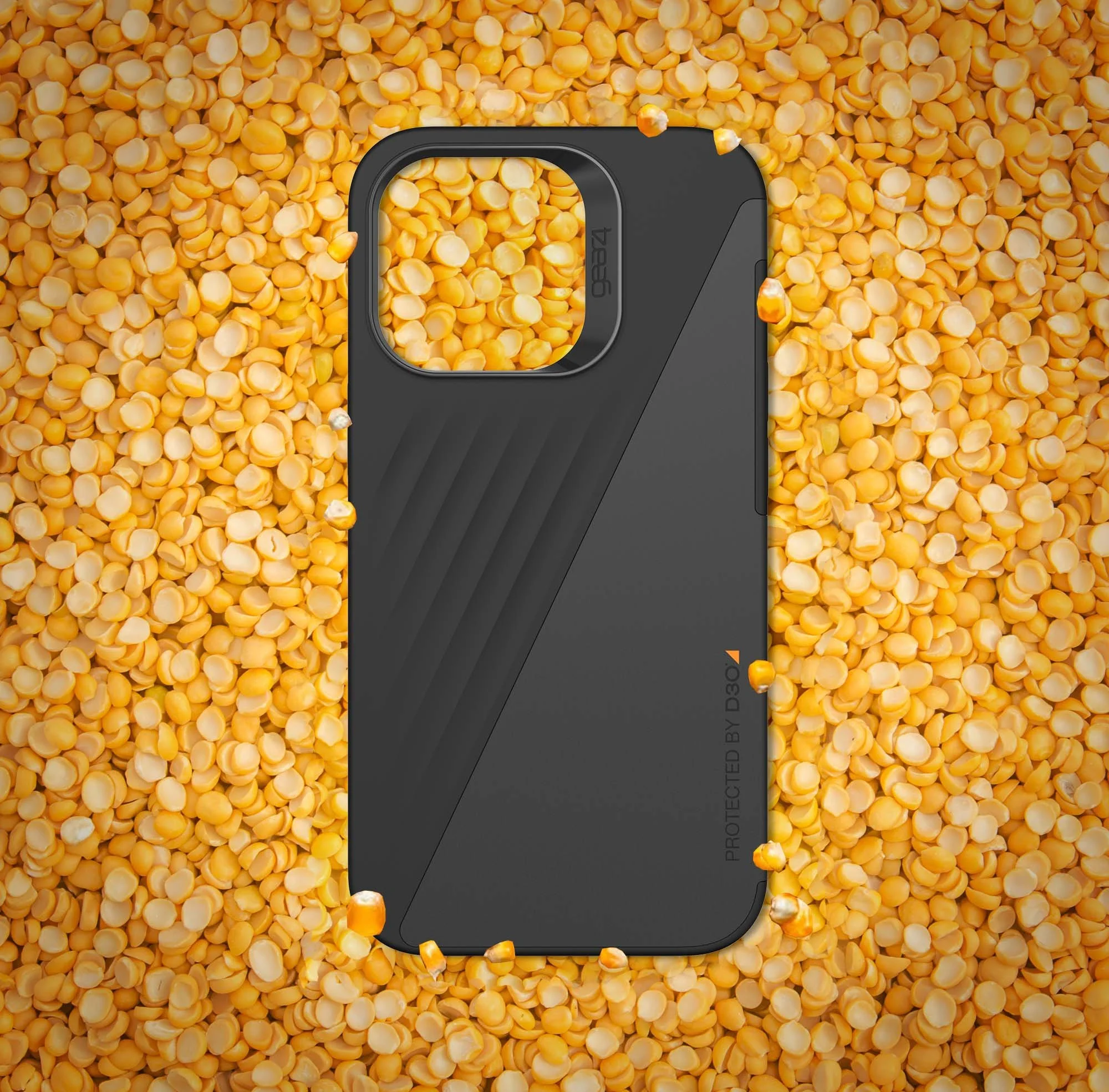 Close-up of a black electronic device, possibly a camera, placed on a large pile of yellow split peas.