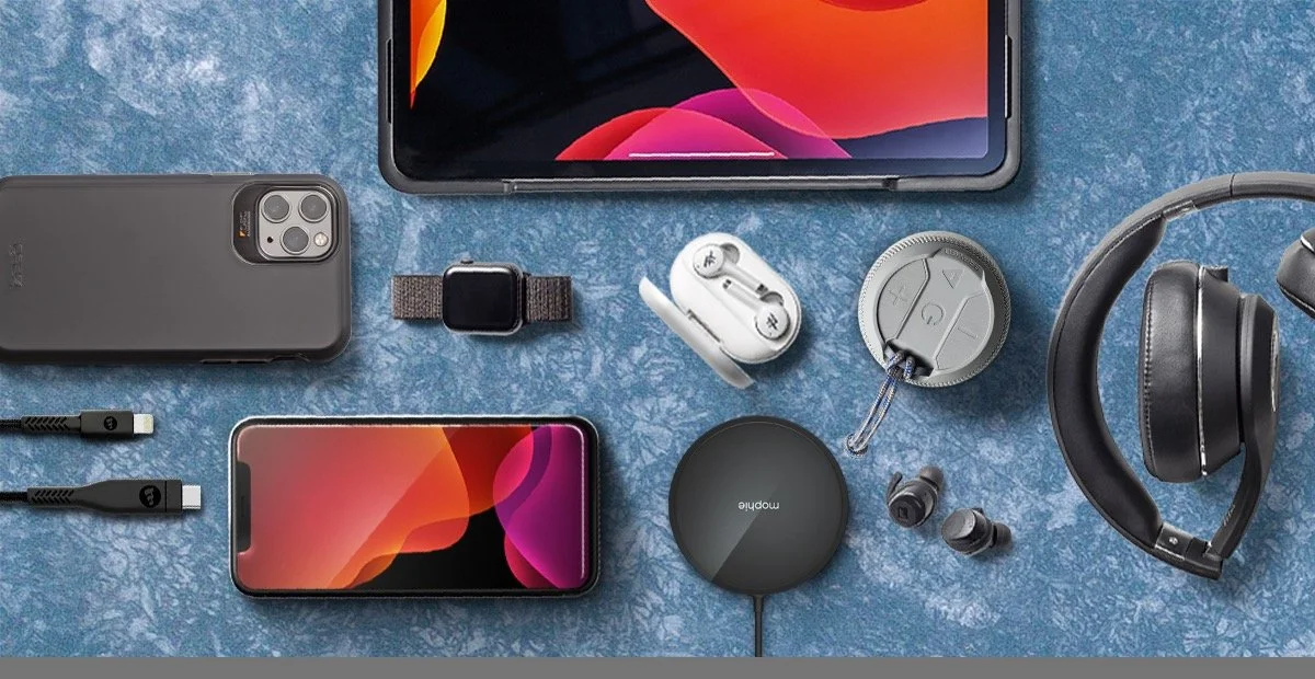 Collection of electronic devices including a smartphone, tablet, wireless earbuds, smartwatch, headphones, portable speaker, charging cables, and a small round device, all laid out on a blue textured surface.