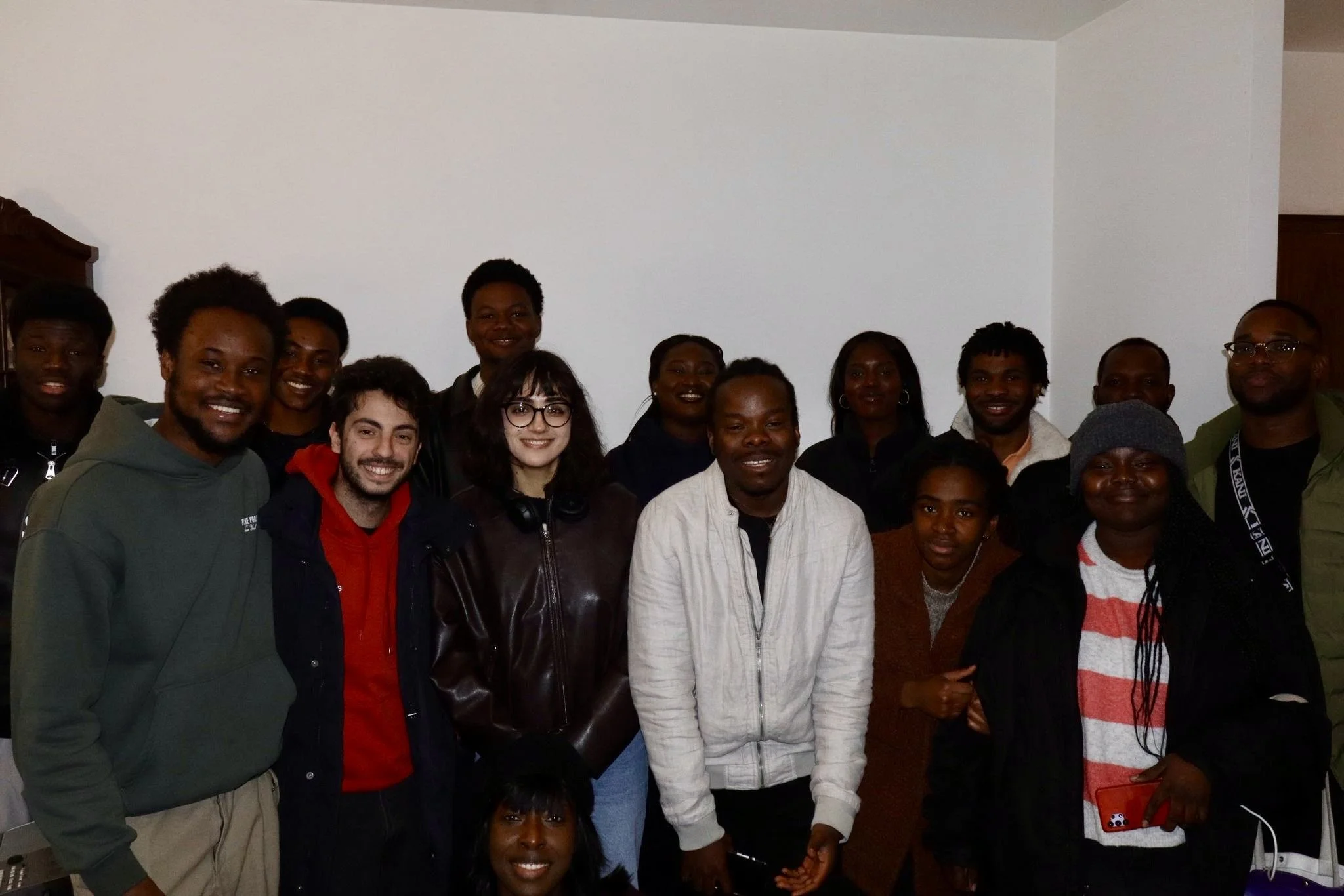 A group of diverse people smiling in a room with white walls.