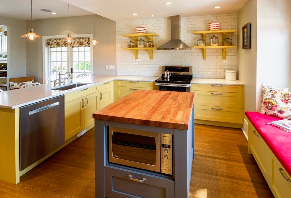Kitchen with yellow cabinets, a wooden island, open shelving, stainless steel appliances, and a window seat with a red cushion and floral pillow.