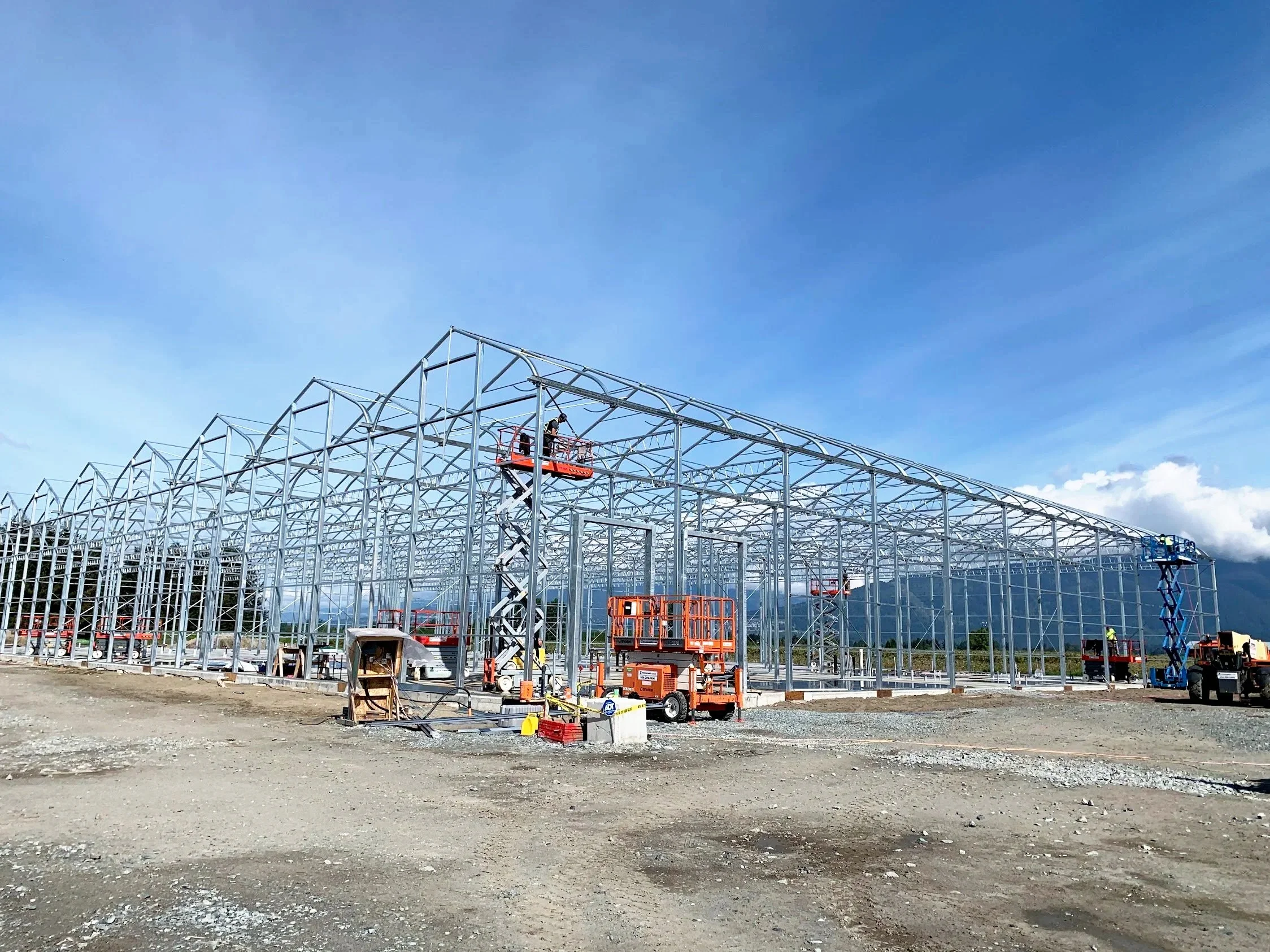 Under construction steel framework for a building with construction equipment and workers, set against a blue sky with some clouds.