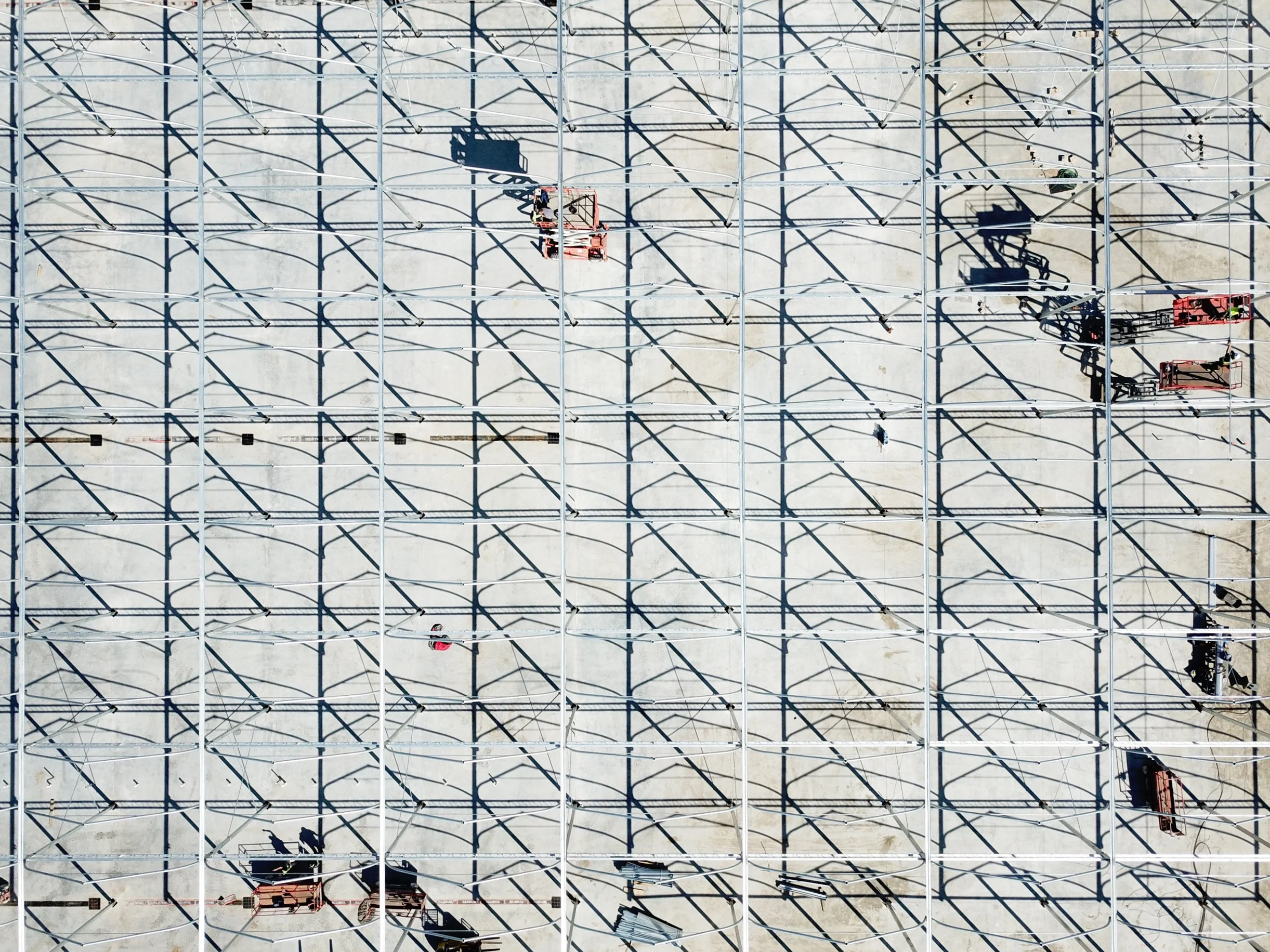 An aerial view of a construction site with workers and equipment working on metal framework and scaffolding.