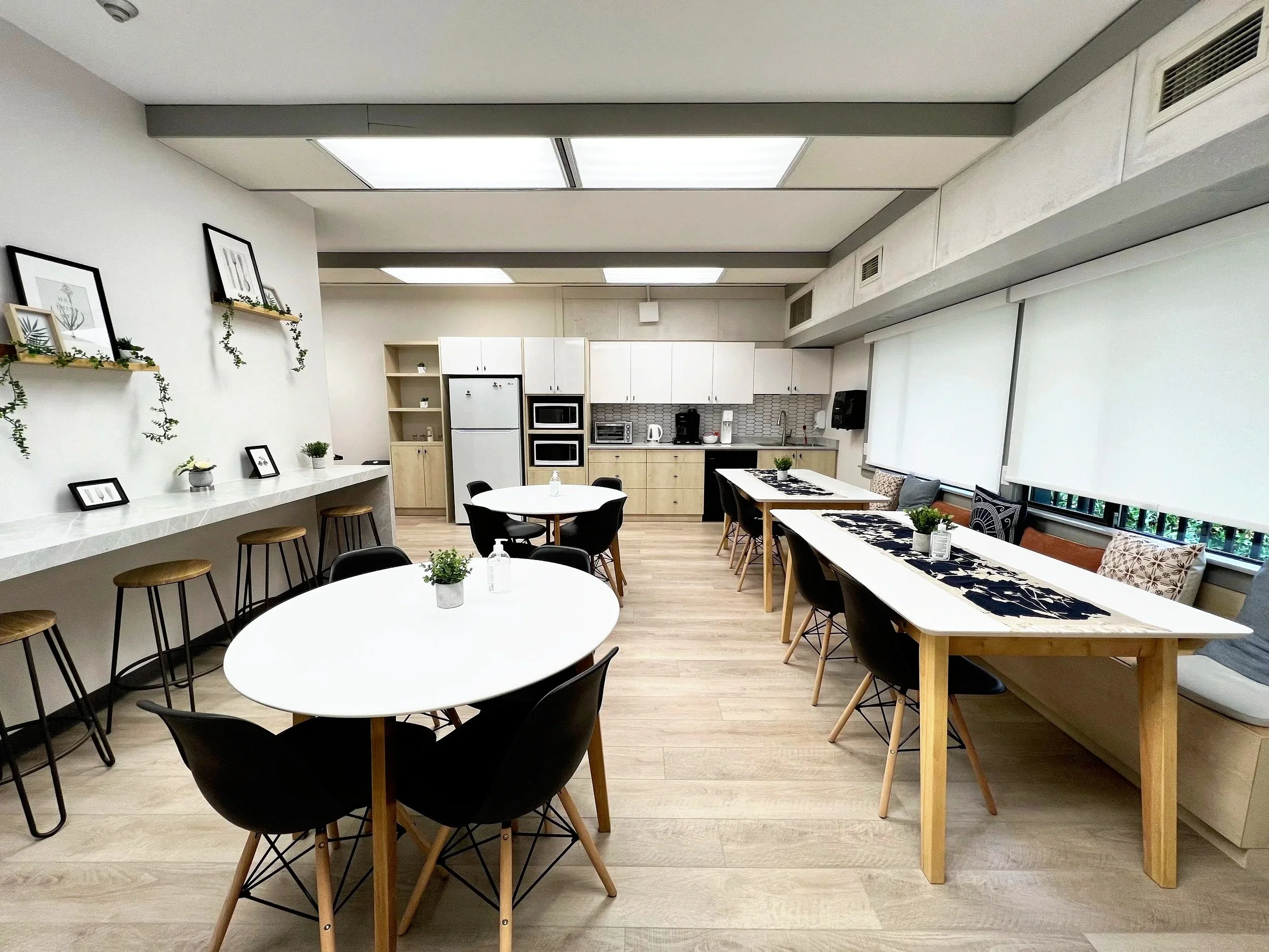 A modern, brightly lit kitchen and dining area with white cabinets, black chairs around round tables, decorative wall art, and wooden accents.