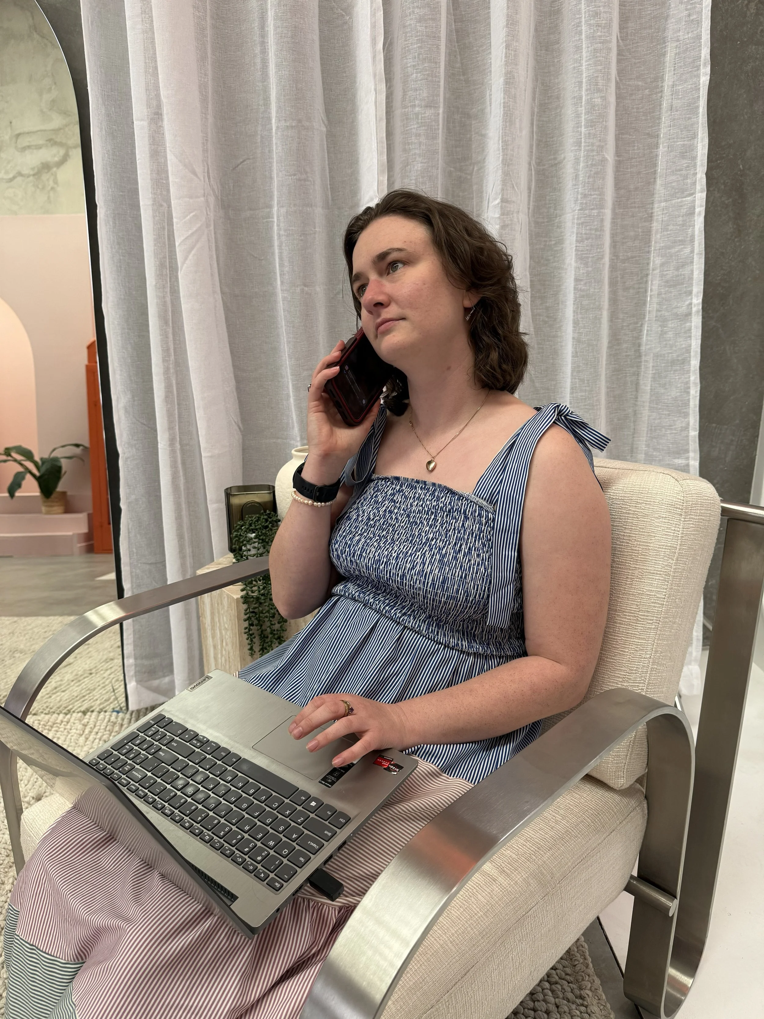 Kate nutritionist sitting on a chair on the phone working on her laptop