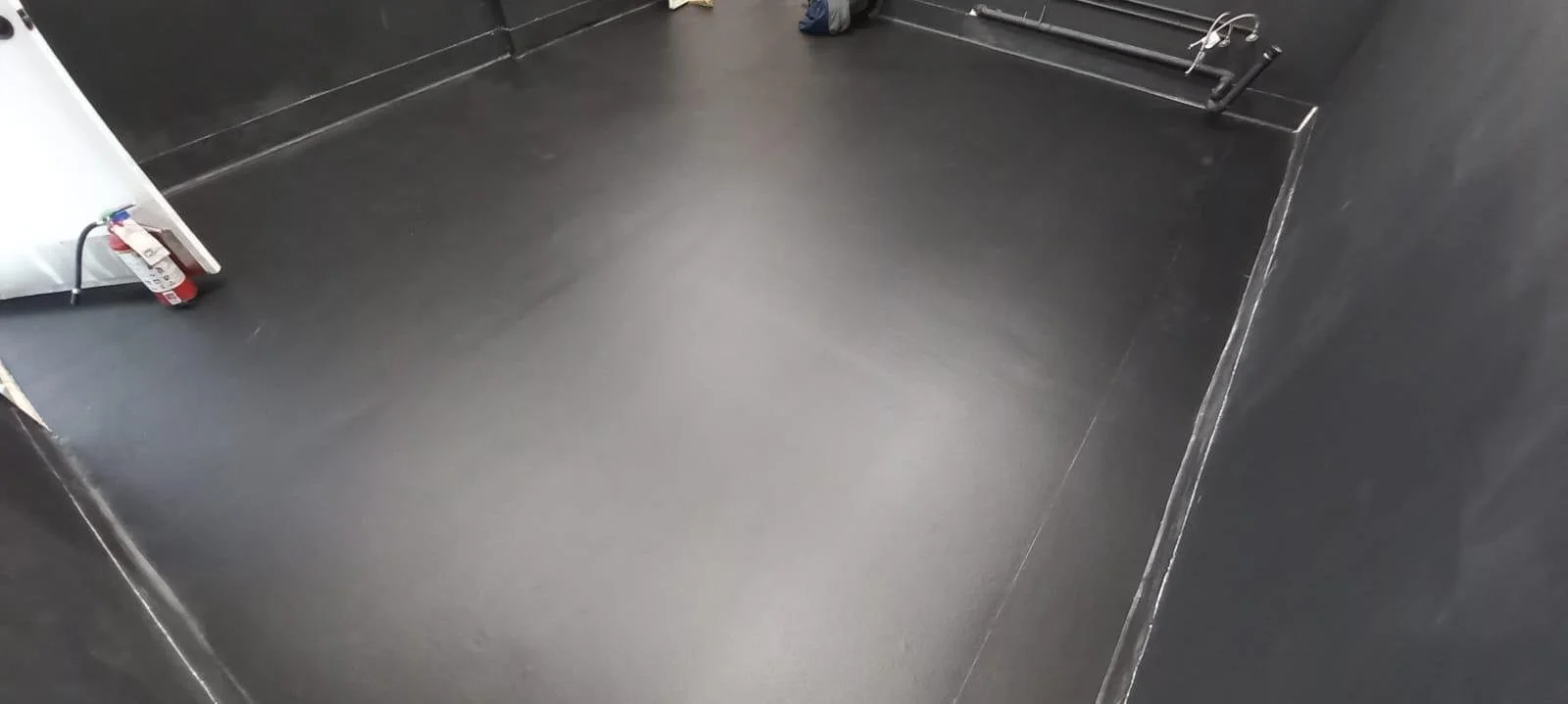 The interior of an empty elevator with black walls and floor, a fire extinguisher on the left side, and some electrical wires in the corner.