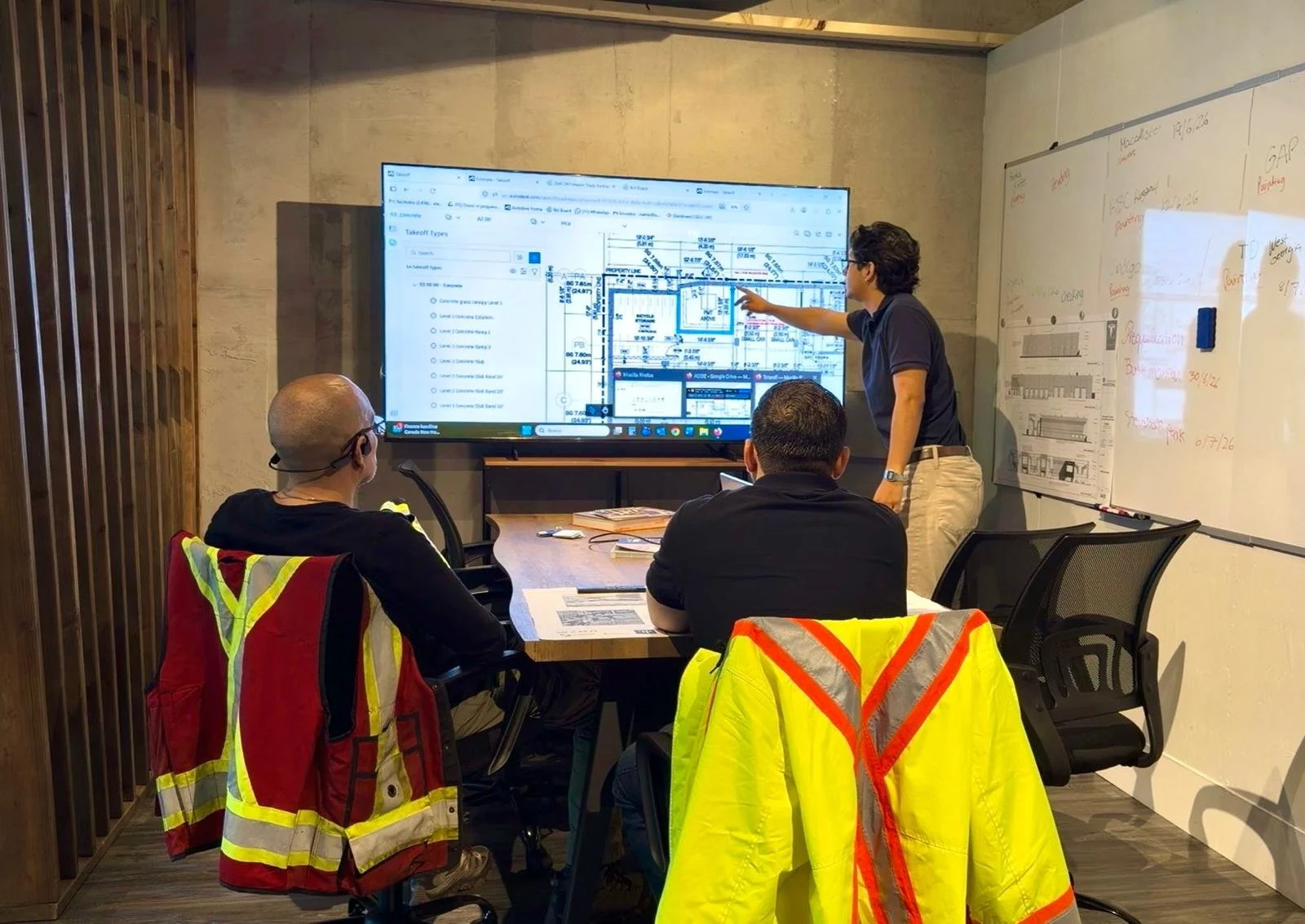 A person with light skin and fair hair is writing on an architectural blueprint or technical drawing with a black pen, with a blurred background that appears to be an industrial or workshop setting.