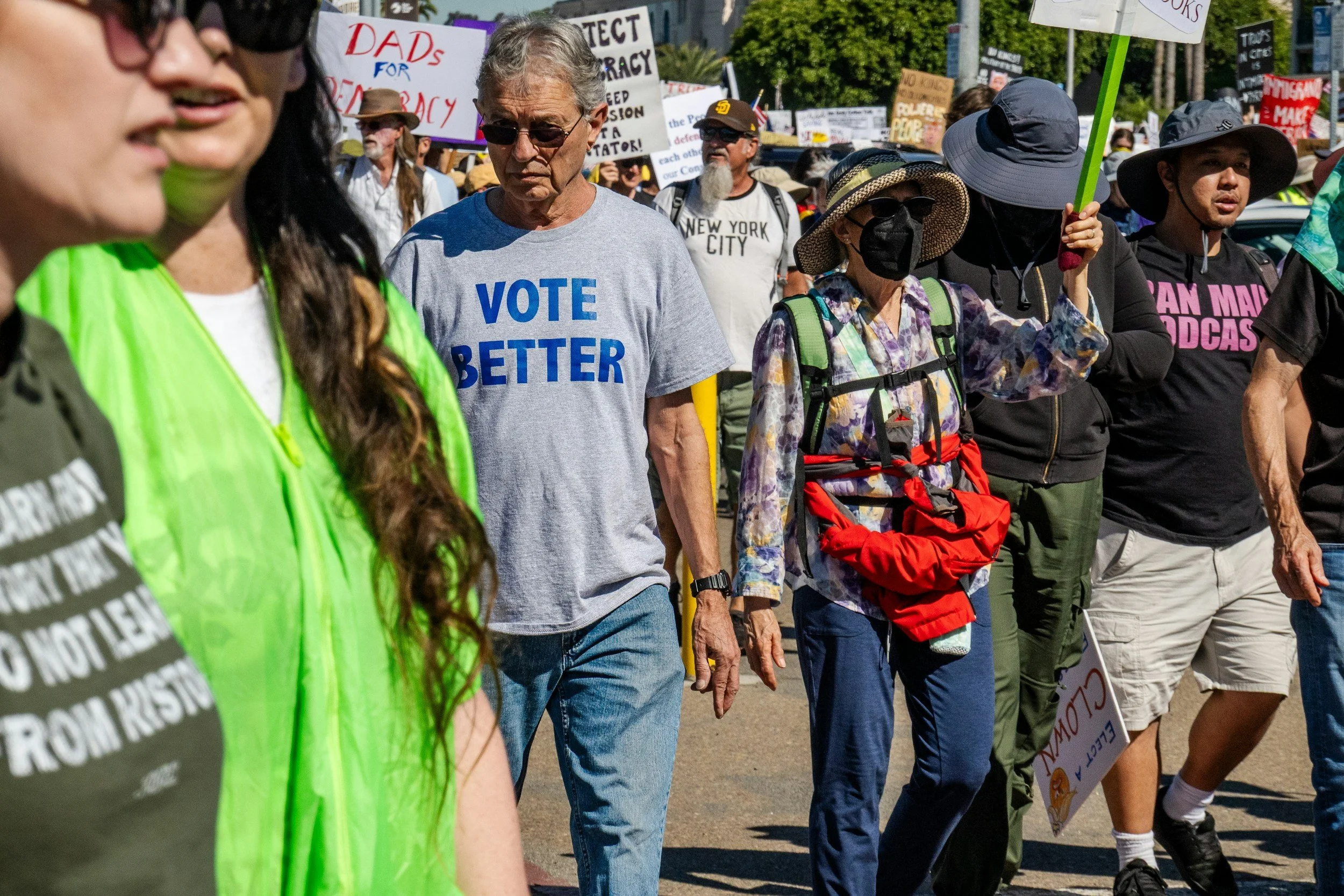 Crowd of people participating in a protest march, holding signs with messages advocating for voter rights, democracy, and political change, outdoors on a sunny day.