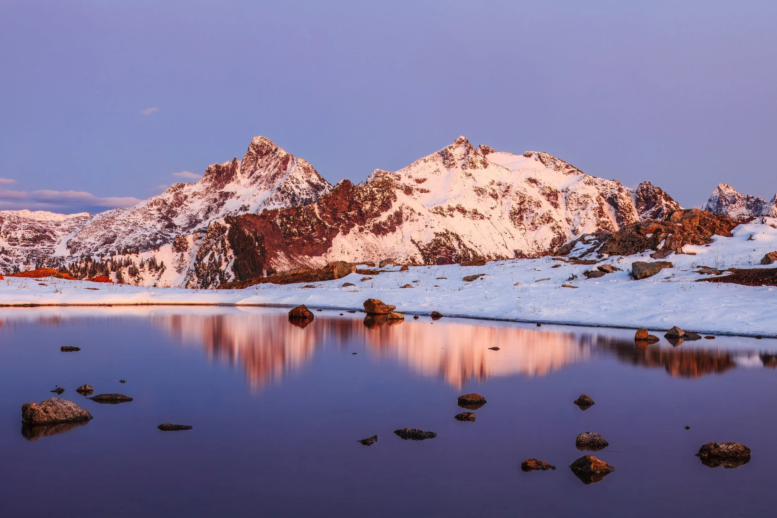 This is textbook alpenglow — that brief window just after sunset (or just before sunrise) when the sun is below the horizon but still lighting the highest peaks from below. The warm coral and salmon tones raking across the snowfields contrast beautif