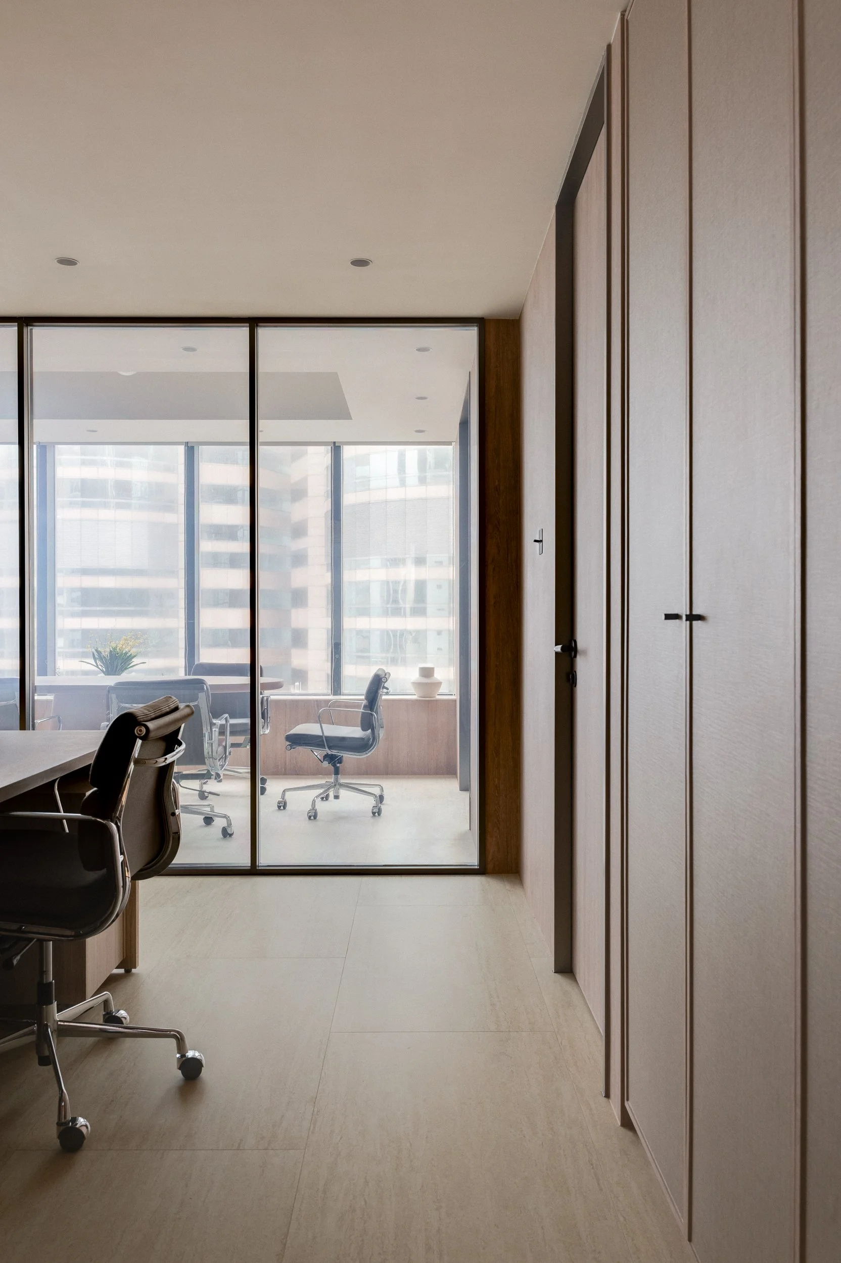 Modern office conference room with glass walls, office chairs, and a large table, overlooking city buildings through large windows.