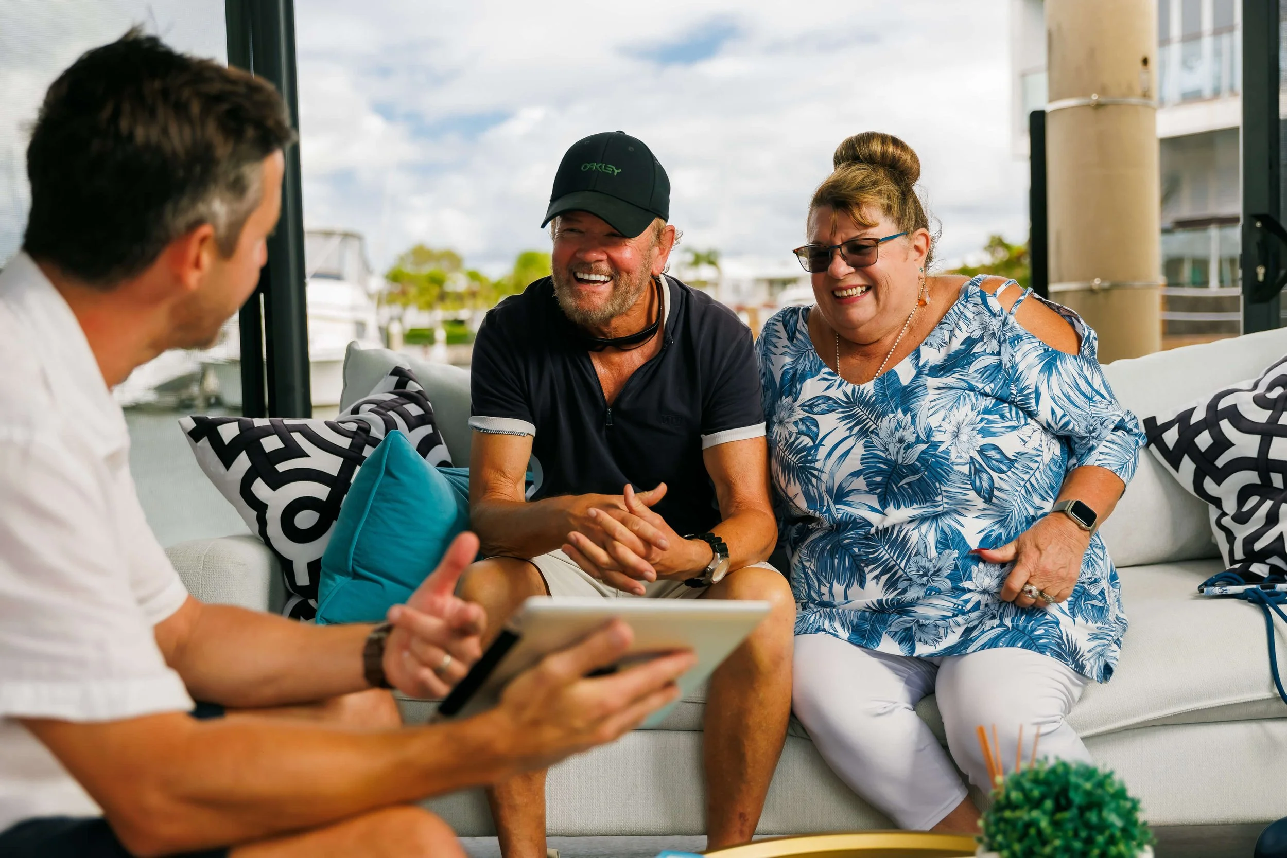 A group of four people sitting in an office, having a conversation and laughing with a marina and boats in the background.