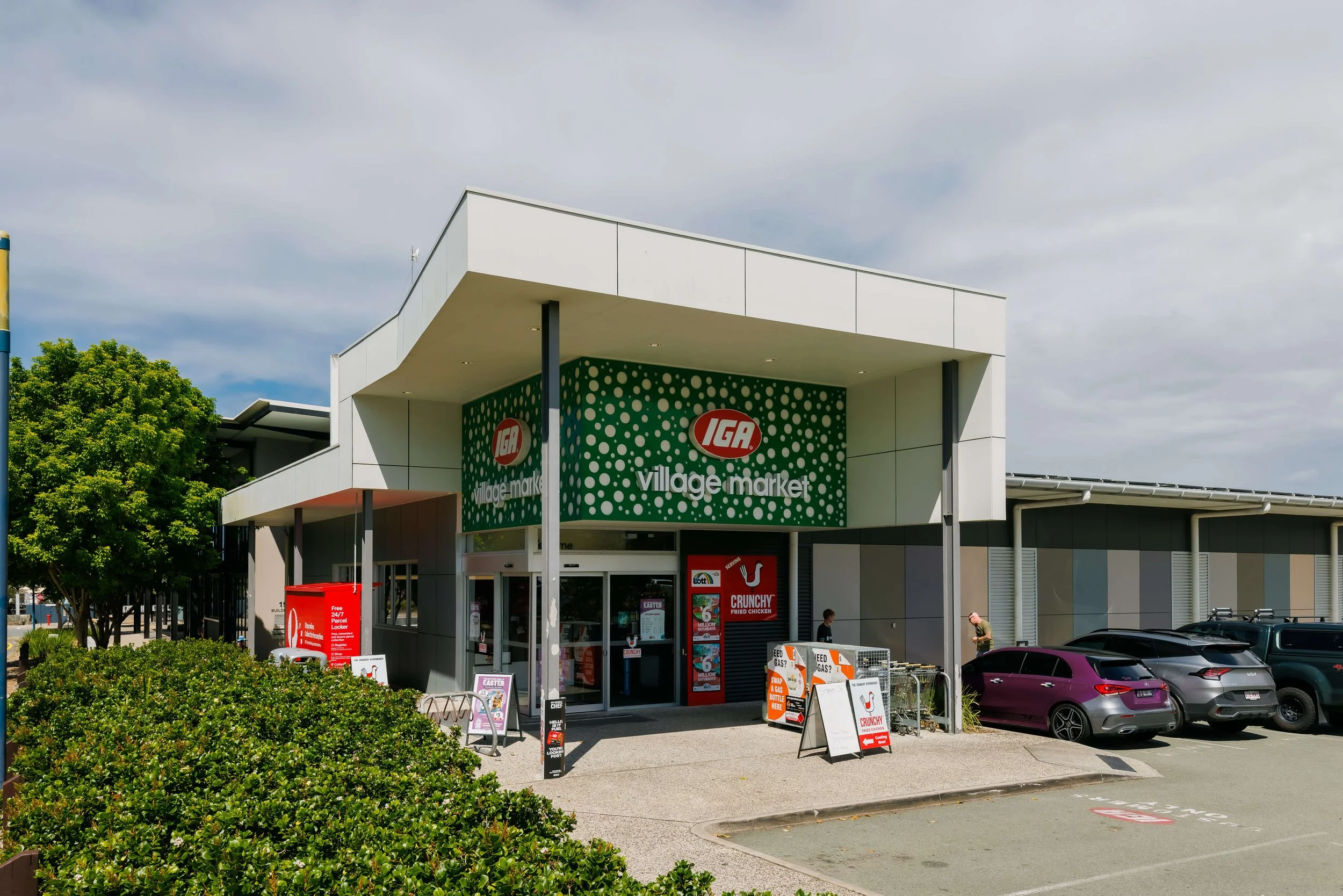 Exterior view of an IGA store with seating outside, parking lot and trees.
