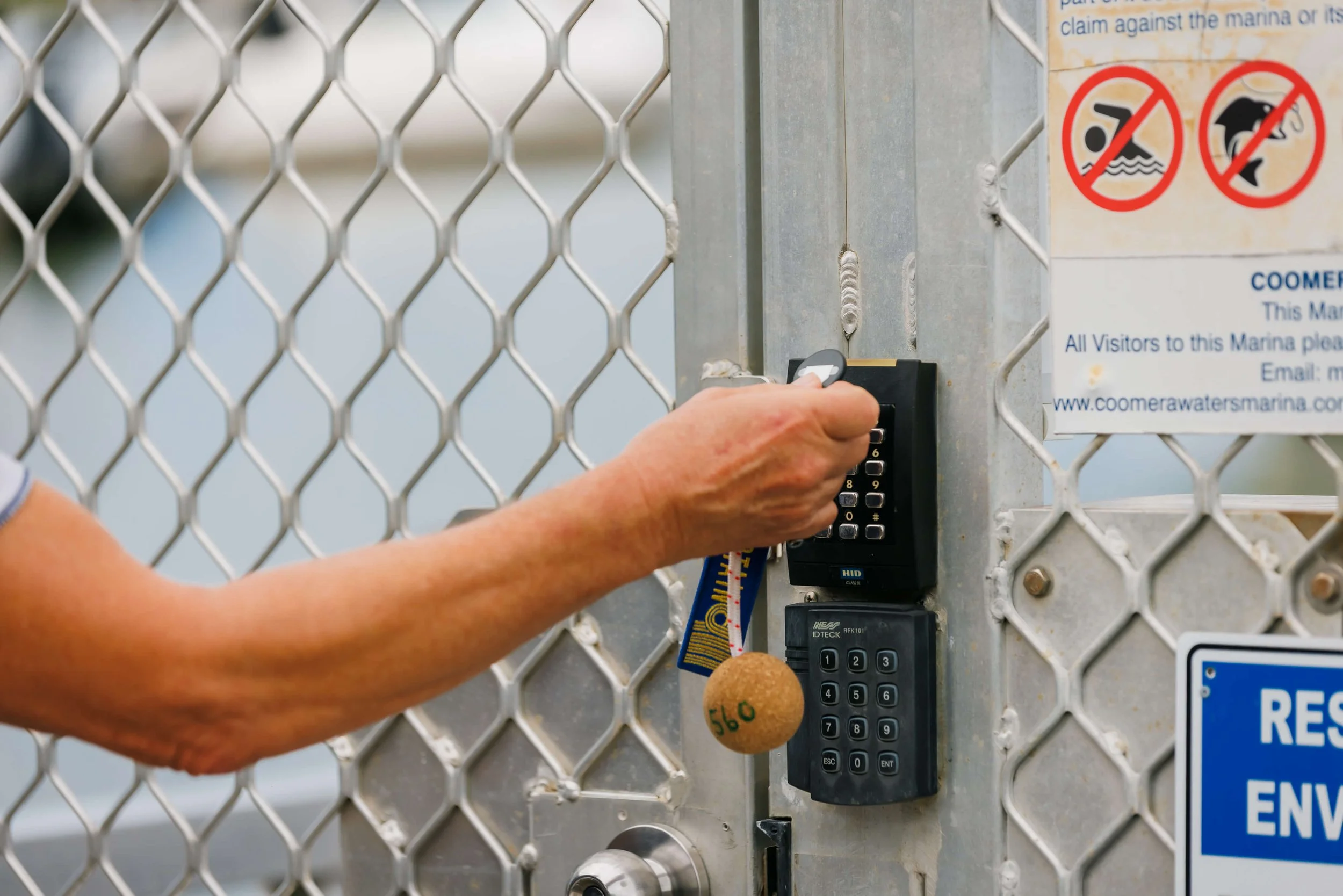 Person entering a code on a keypad at a secure gate with signs prohibiting swimming and diving.