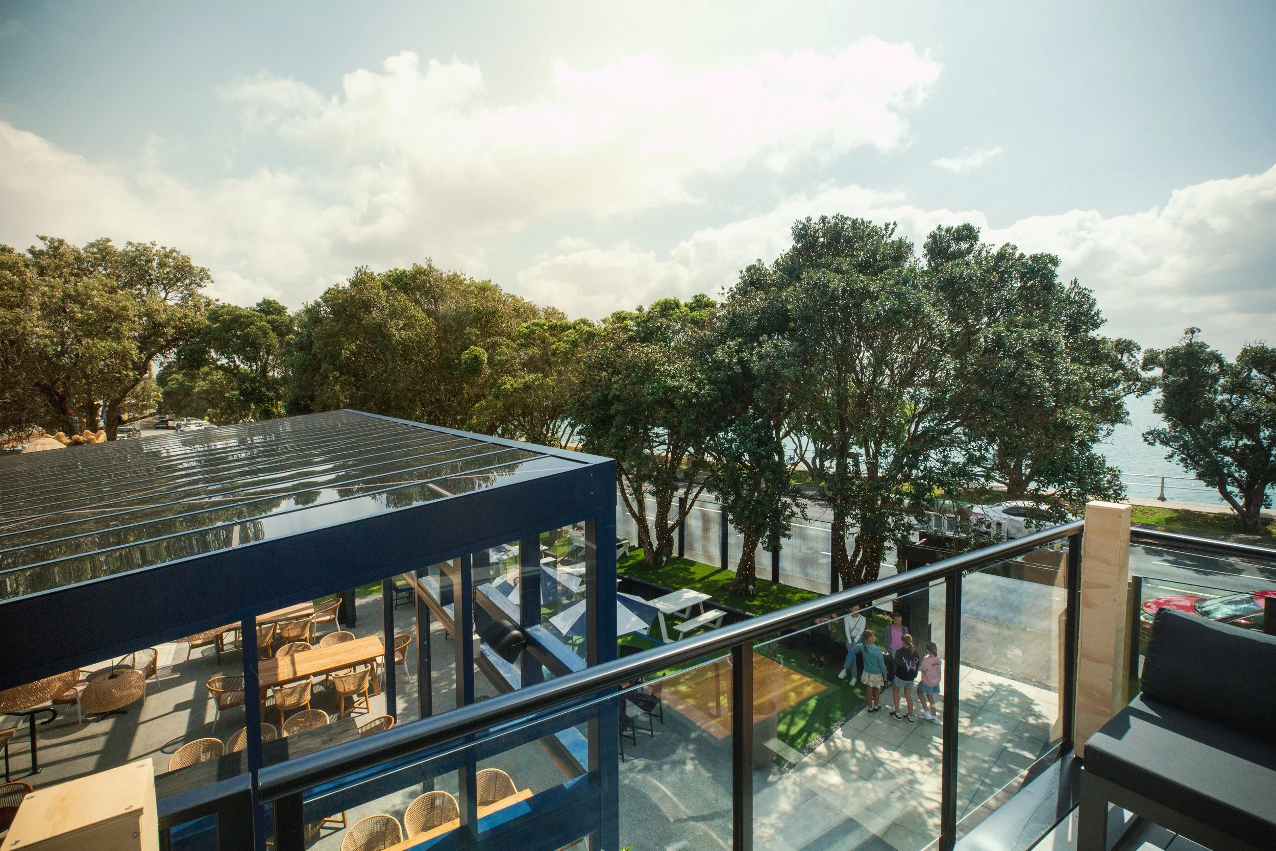 A view from a balcony overlooking a parking lot, tall trees, and a partly cloudy sky during daytime.