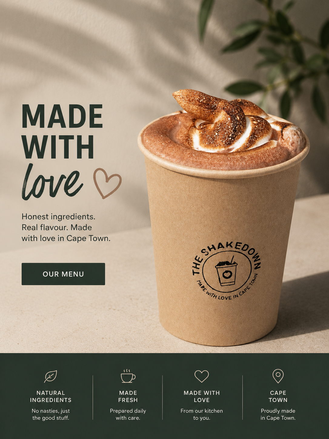 A paper cup with a logo of a coffee cup with a heart, filled with hot chocolate topped with whipped cream and a toasted marshmallow. The background has green leaves and a light-colored surface.