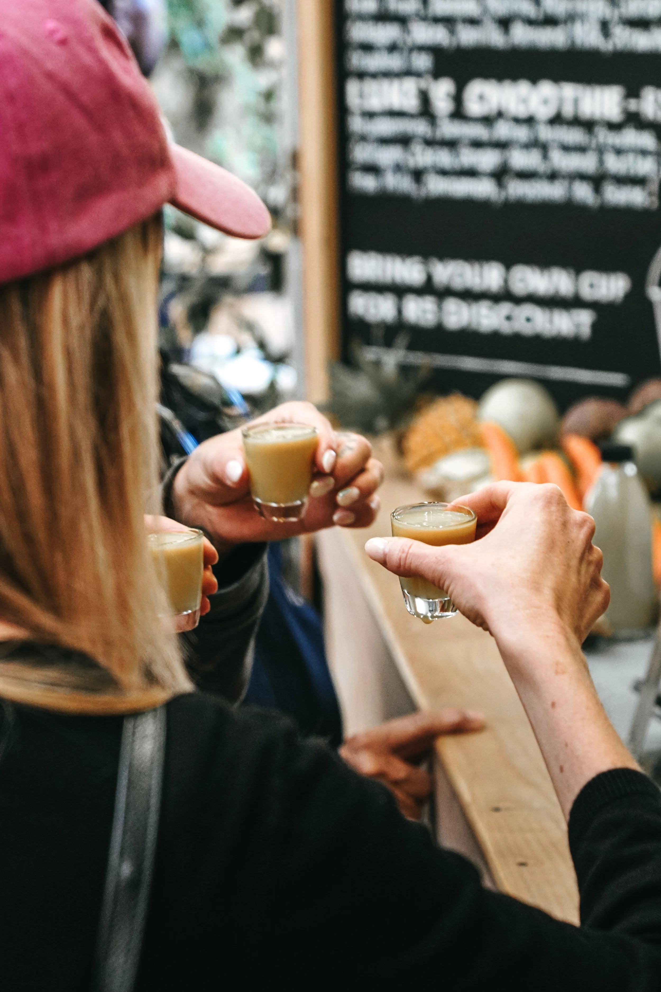 People holding small glasses of a light-colored beverage in a casual setting, possibly at a bar or tasting event.