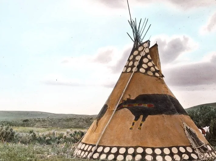Native American tipi with painted horse design in a rural landscape.
