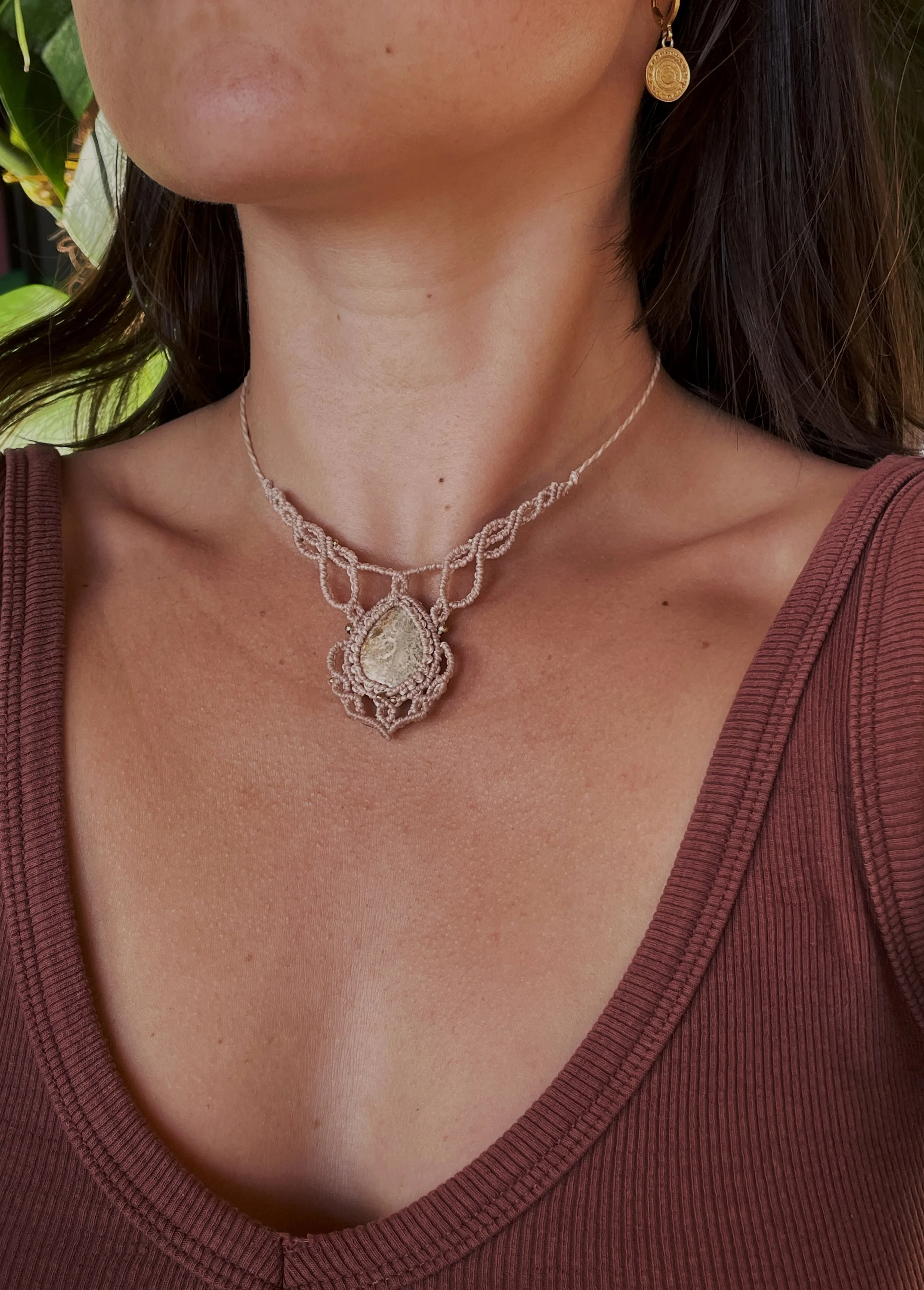 Close-up of a woman wearing a pearl necklace with a large pendant and a gold earring, showing her neck and part of her chest, dressed in a V-neck maroon top. She has a fair skin tone and dark hair.