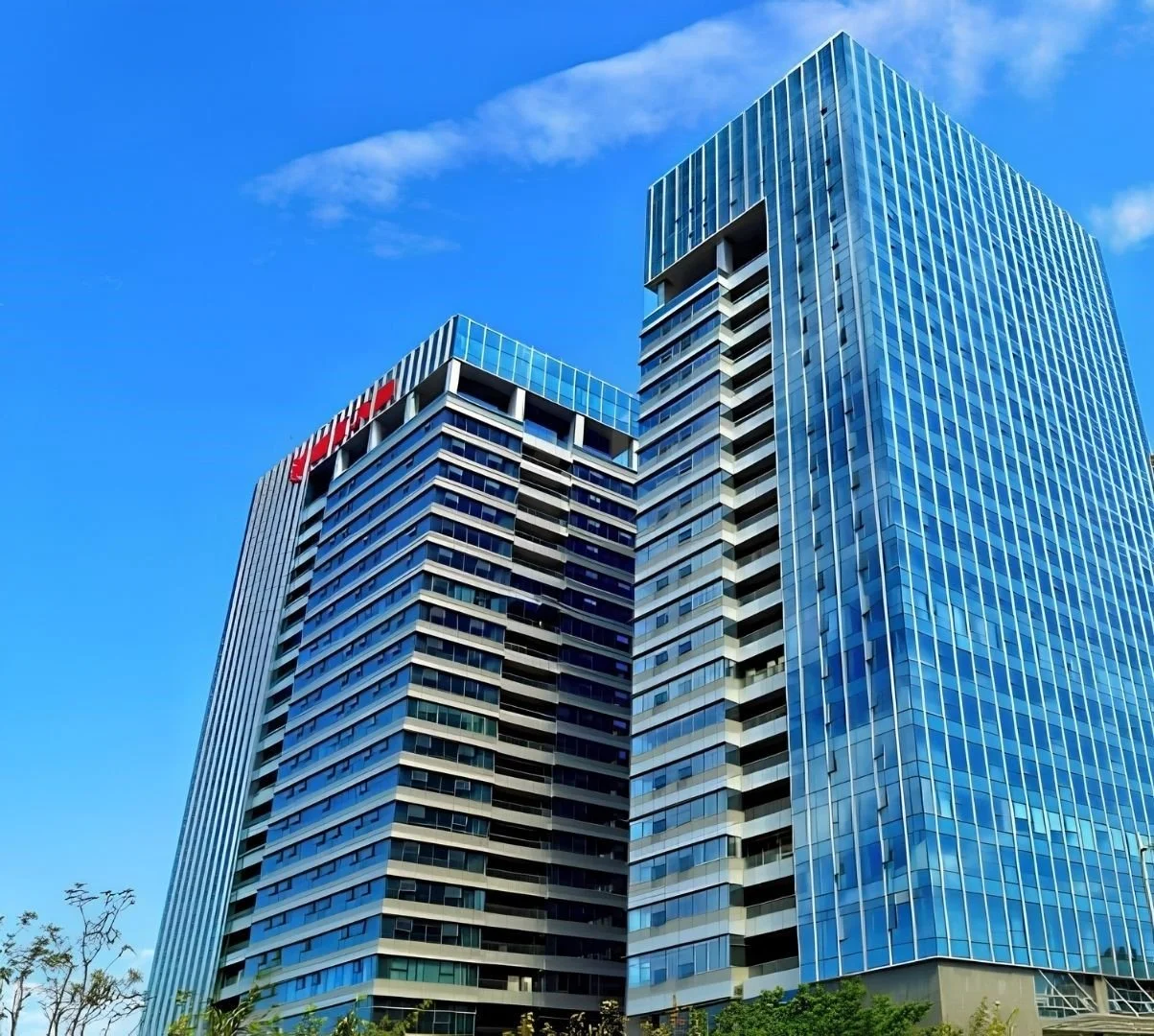 Two modern high-rise office buildings with glass facades in a city under a blue sky