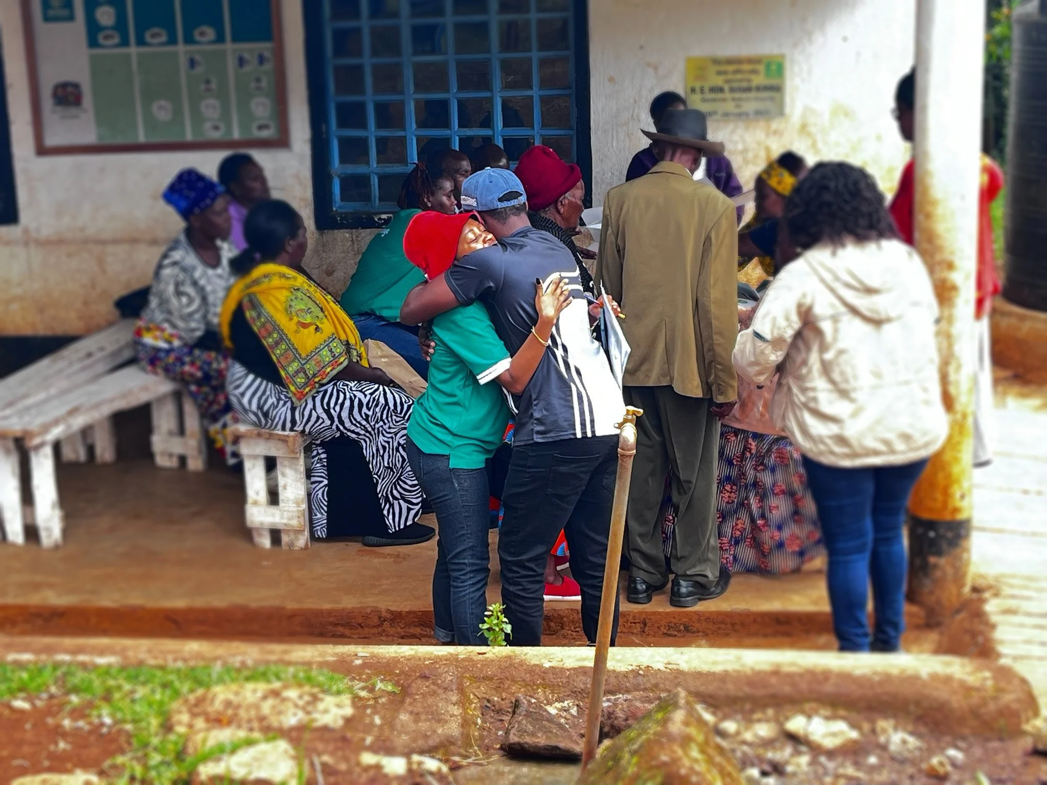 A group of people sitting and standing outside a building; some are talking, and the scene appears to be a community gathering or meeting.