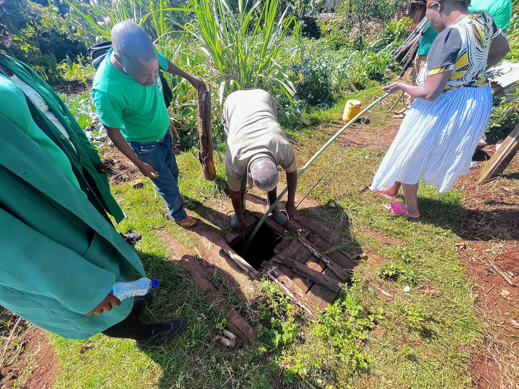 People working outdoors in a garden with lush greenery and plants, planting or tending to the soil.